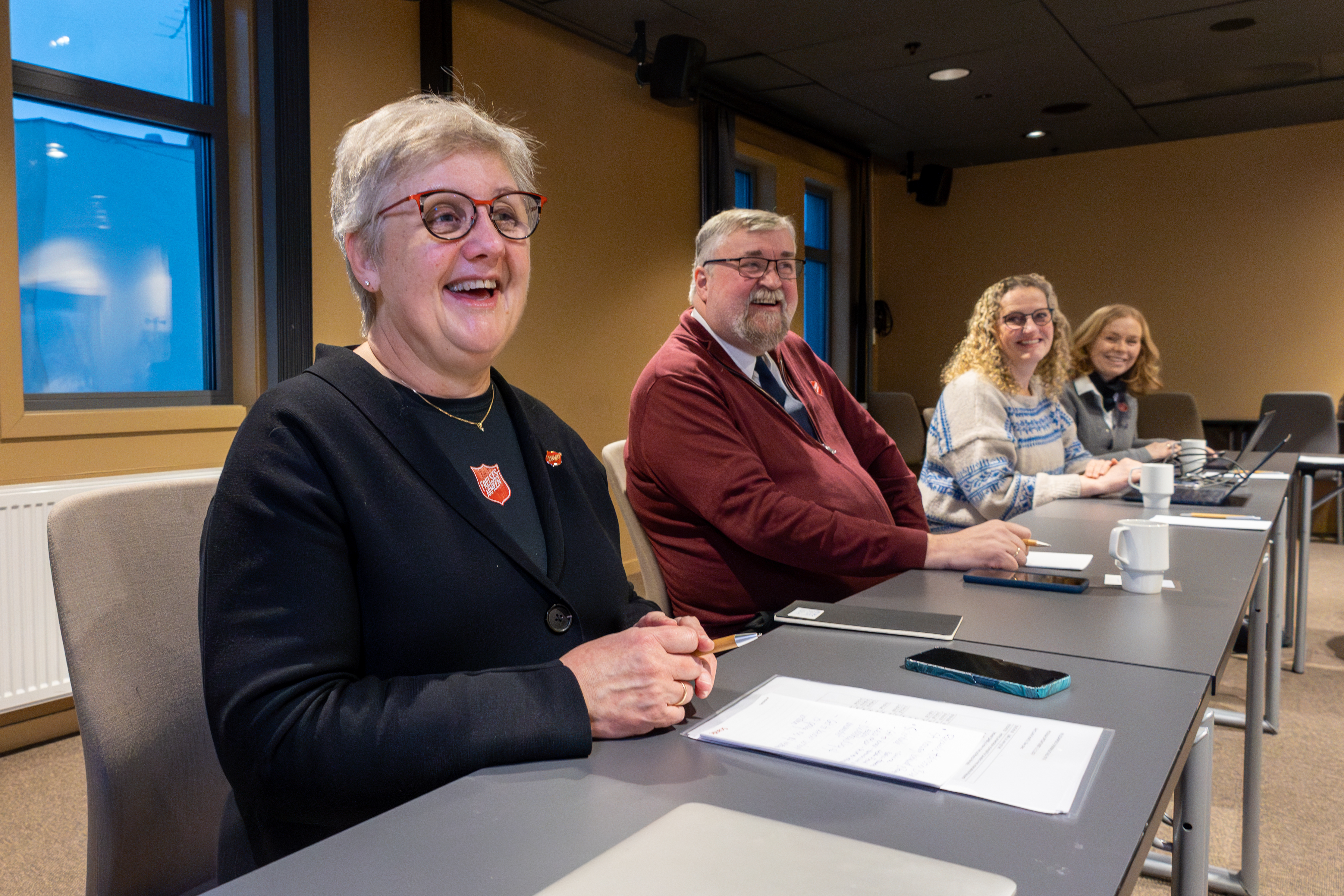 Tre kvinner og én mann sitter ved hver sin pult innover i rommet.