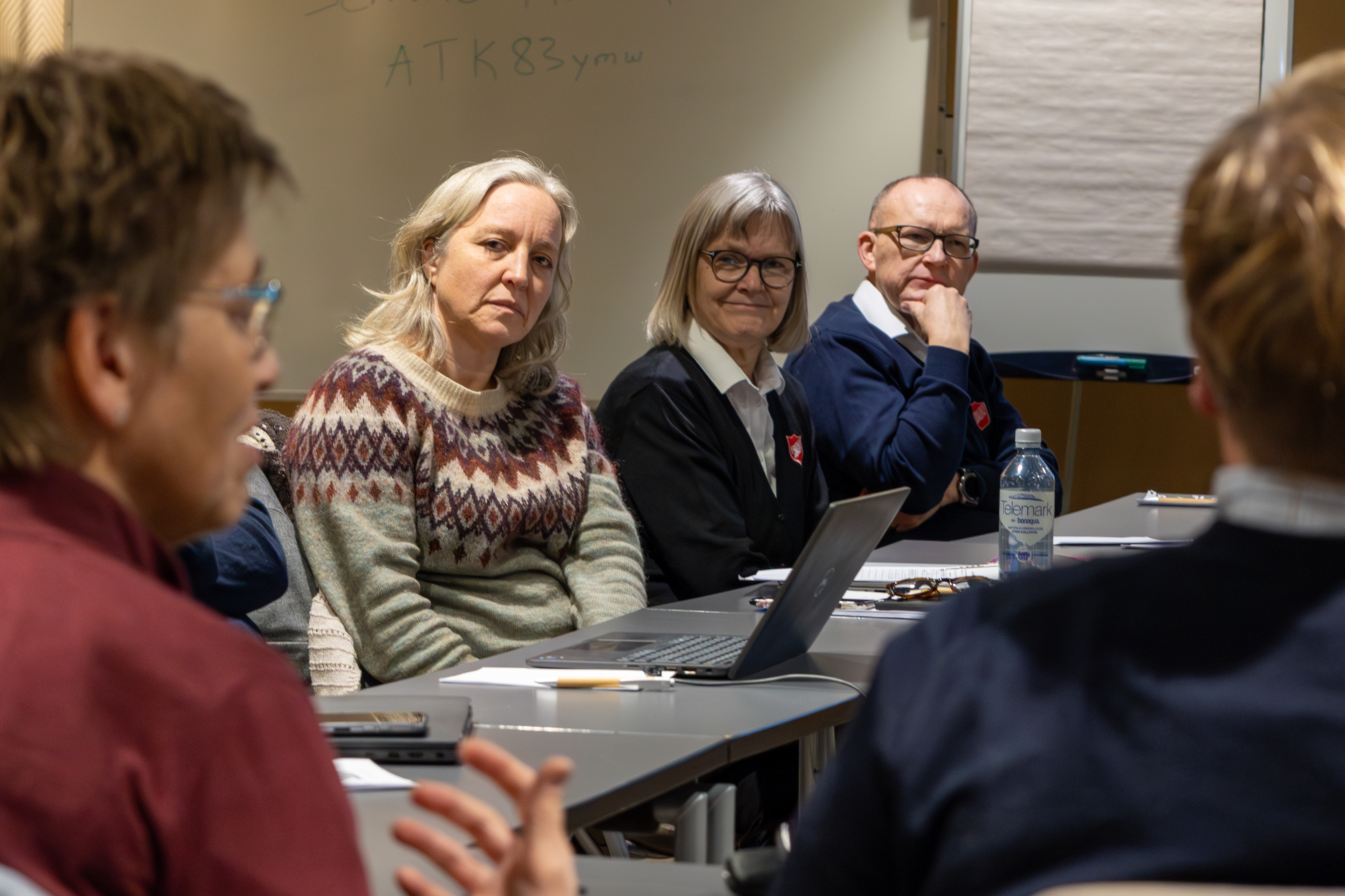 Flere personer sitter i en ring, der tre har på seg uniform fra Frelsesarmeen.