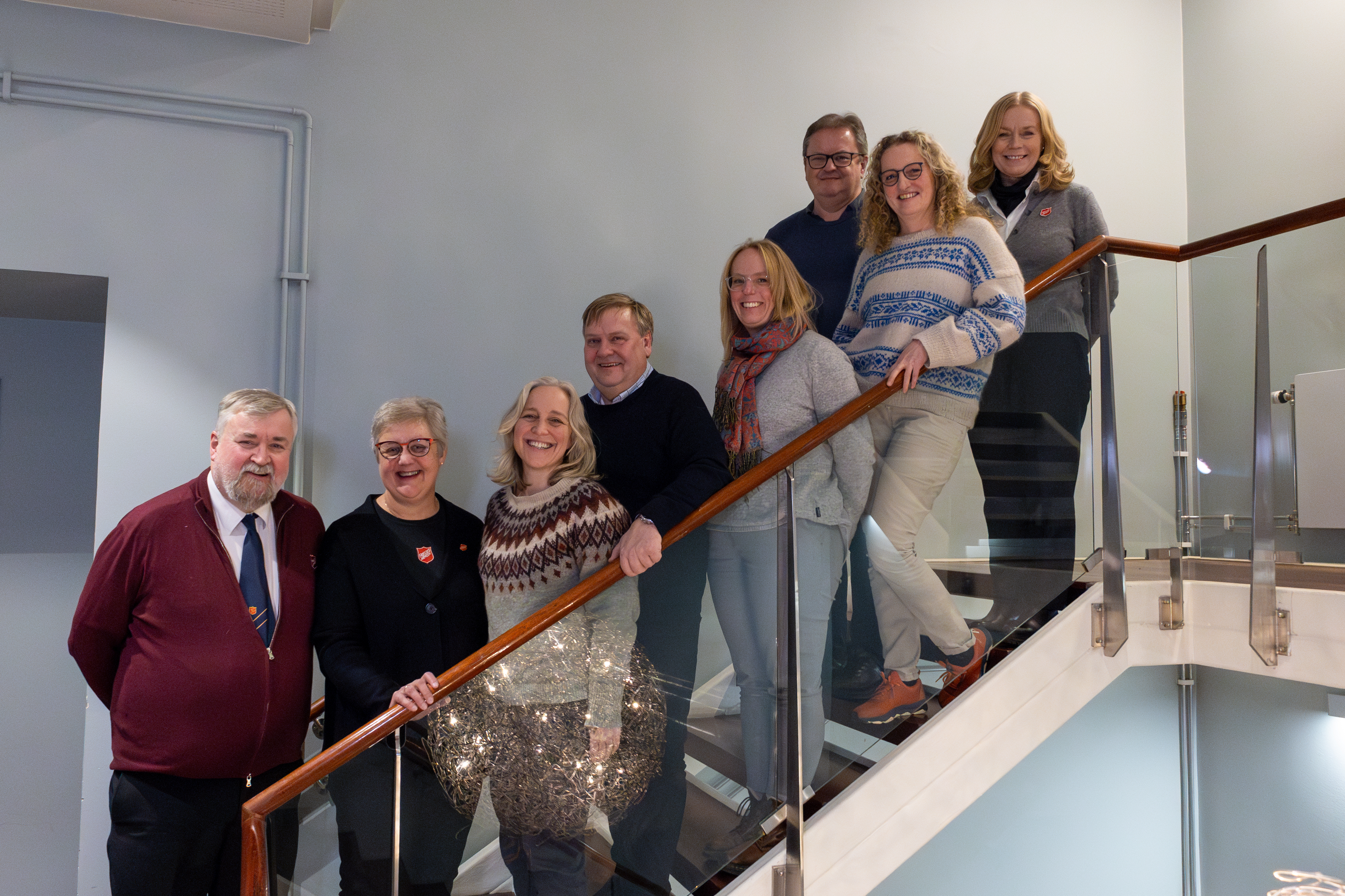 Tre menn og fem kvinner står på en rekke oppover en trapp inne på et hotell.