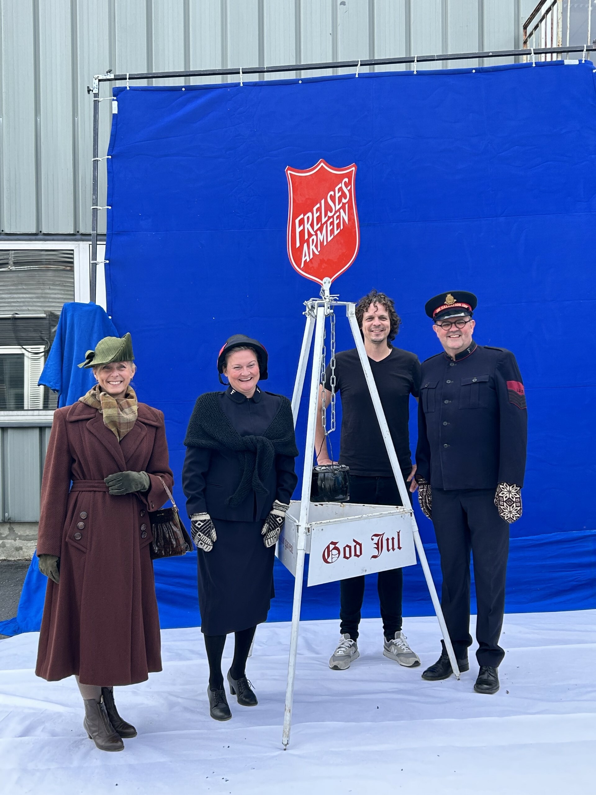 To kvinner og to menn står ved en julegryte. Bak er et blått lerret.