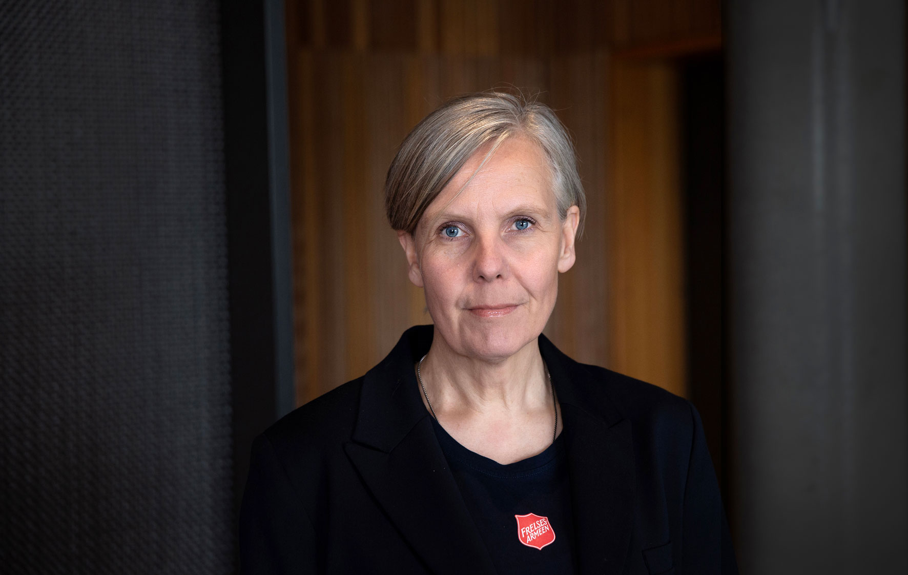 Foto: Kvinne i 50-årene med kort, grått hår. Hun har svarte klær med rødt Frelsesarmé-skjold.