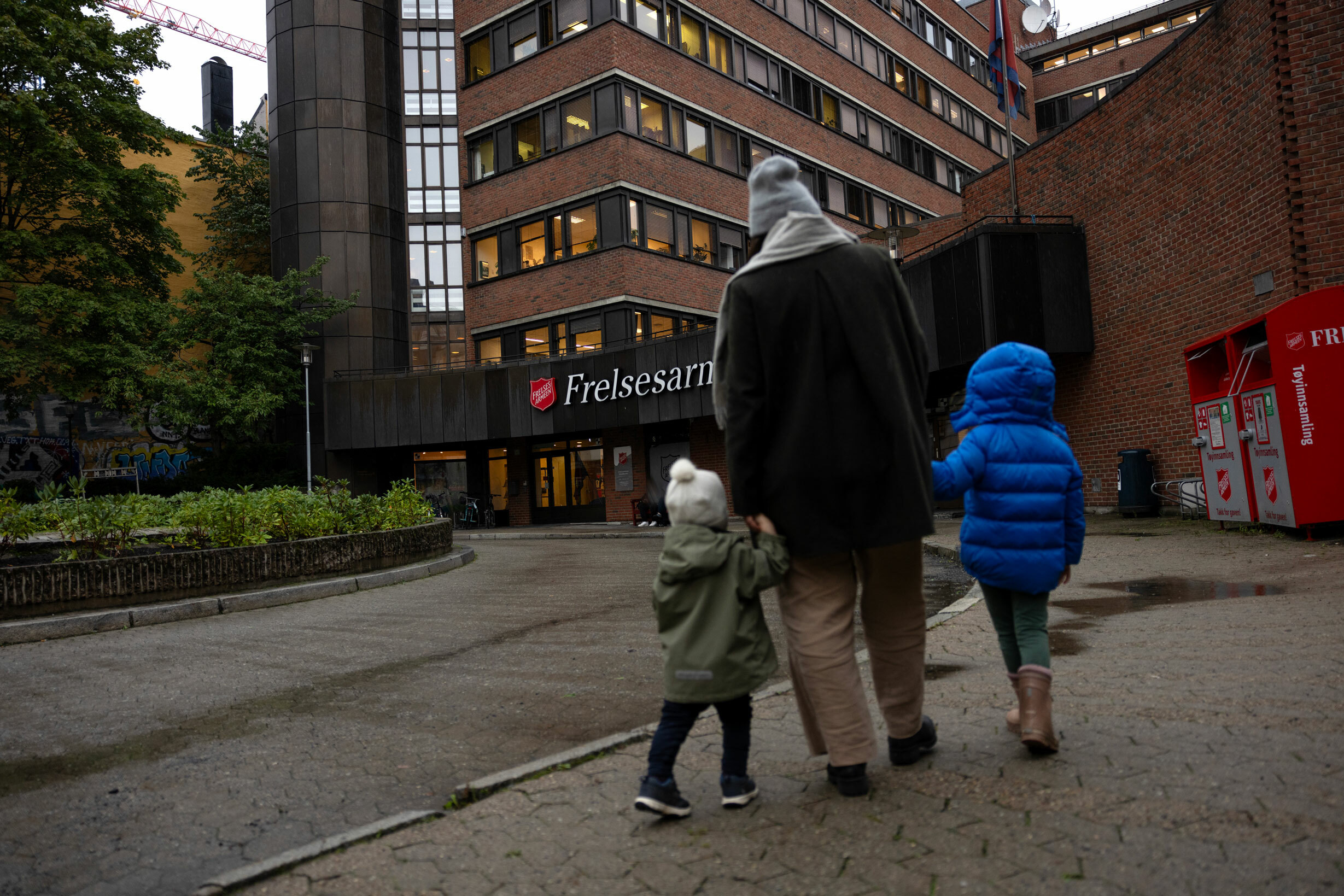 Foto: Kvinne med to barn i barnehagealder og småskolealder, står med ryggen til utenfor et av Frelsesarmeens lokaler i Oslo.