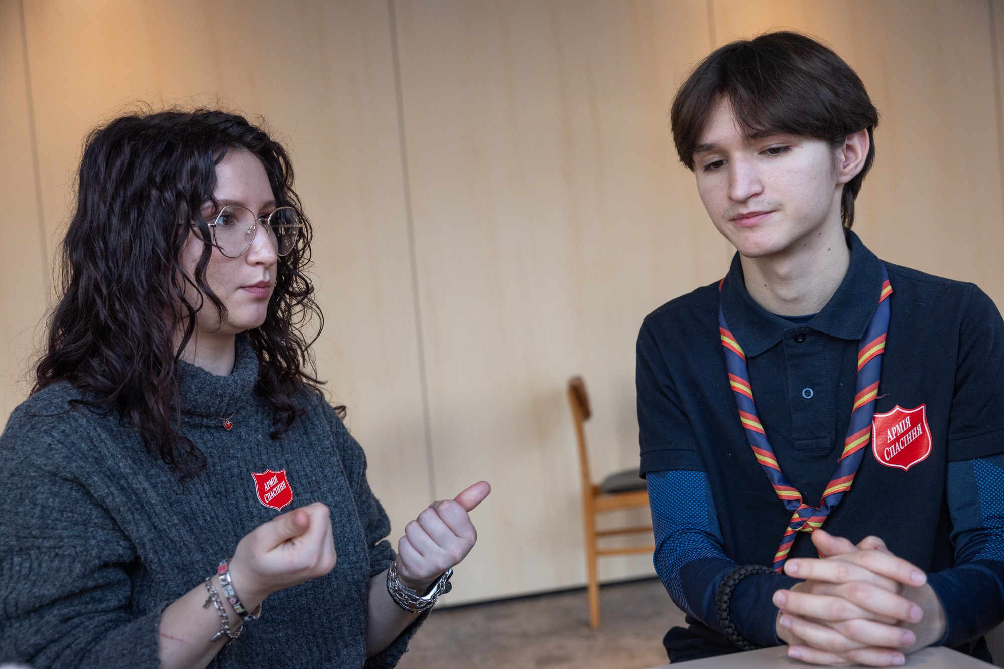 Foto: Ung kvinne med briller og ung mann sitter ved et bord og snakker sammen. Begge har brune øyne og mørkt hår. De ligner på hverandre.