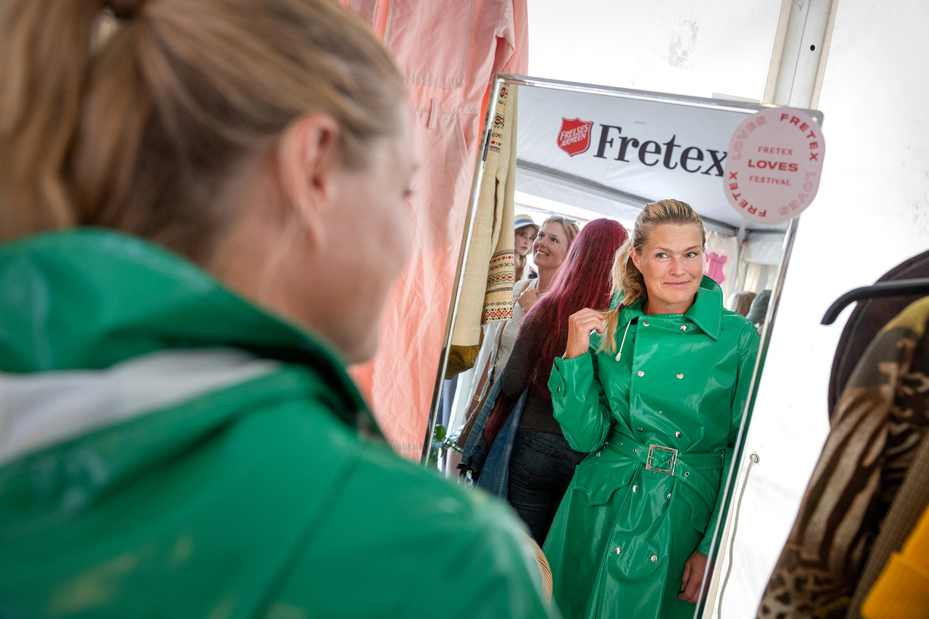 Foto: Kvinne prøver på knall grønn regnfrakk. Ser seg i speilet.