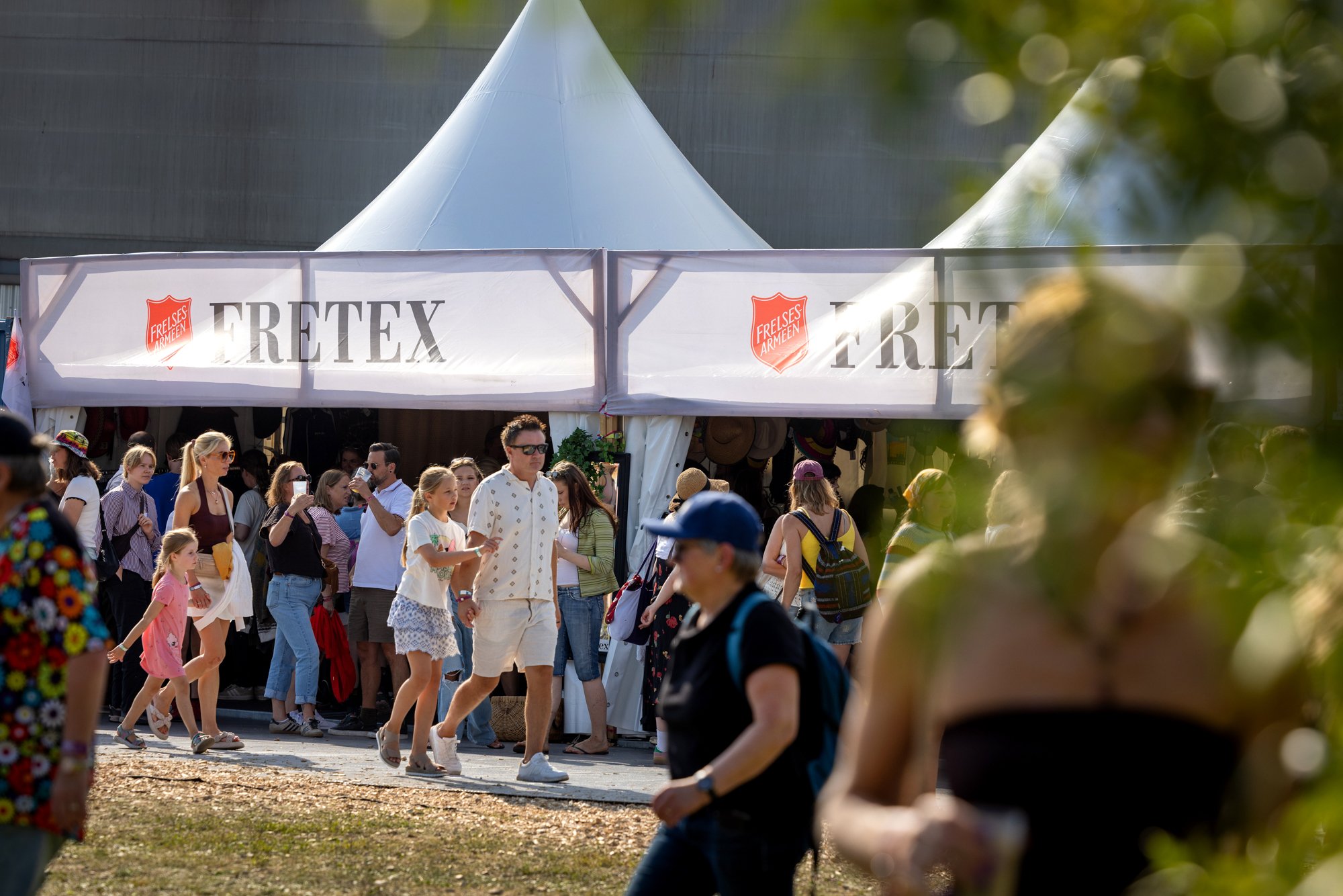 Foto: Hvitt telt med to "spir" og to logoer fra Fretex. Det er mange mennesker som går utenfor på gresset og en grussti.
