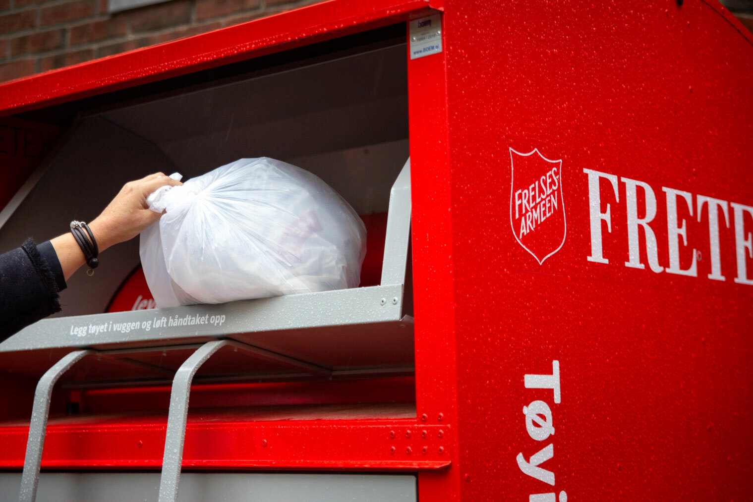 Foto: En hånd som kaster en hvit pose med klær i oppi en rød container fra Fretex.