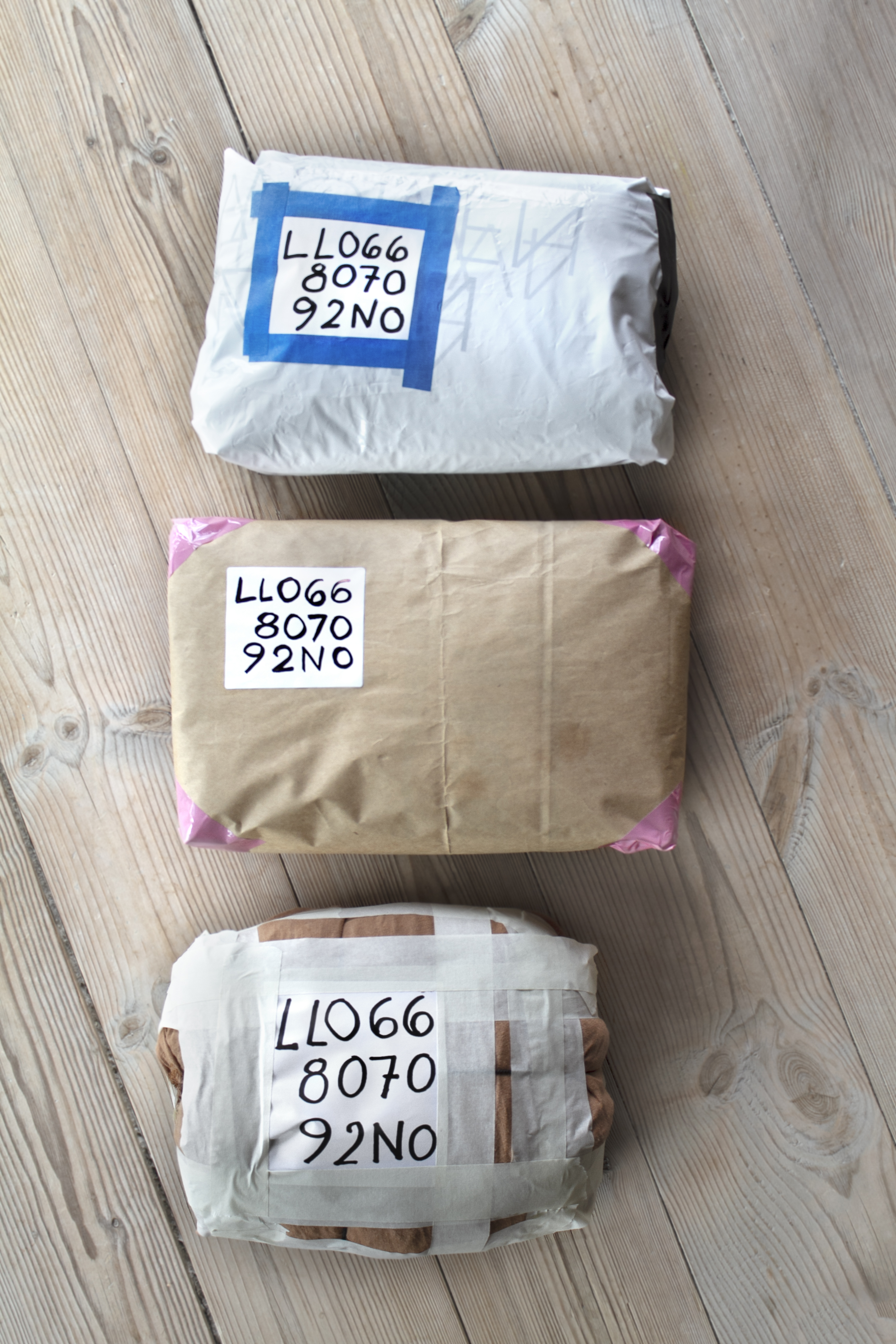 Foto: Høydebilde med tre pakker som ligger på rekke nedover. Alle har en kode skrevet på, men den første er pakket inn i plast, den andre i gråpapir og den siste i tøy med tape surret rundt.