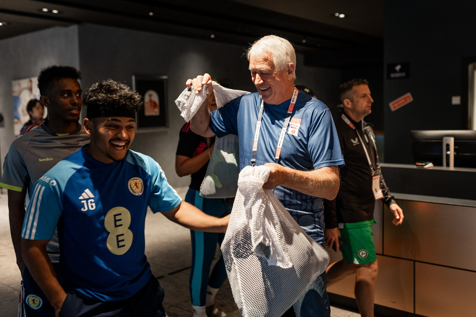 Foto: Steinar i blå hwc-t-skjorte smiler og gir en hvit sekk med klær til en spiller i blå t-skjorte som er på vei forbi ham. Spilleren smiler bredt. I bakgrunnen sees to andre spillere.