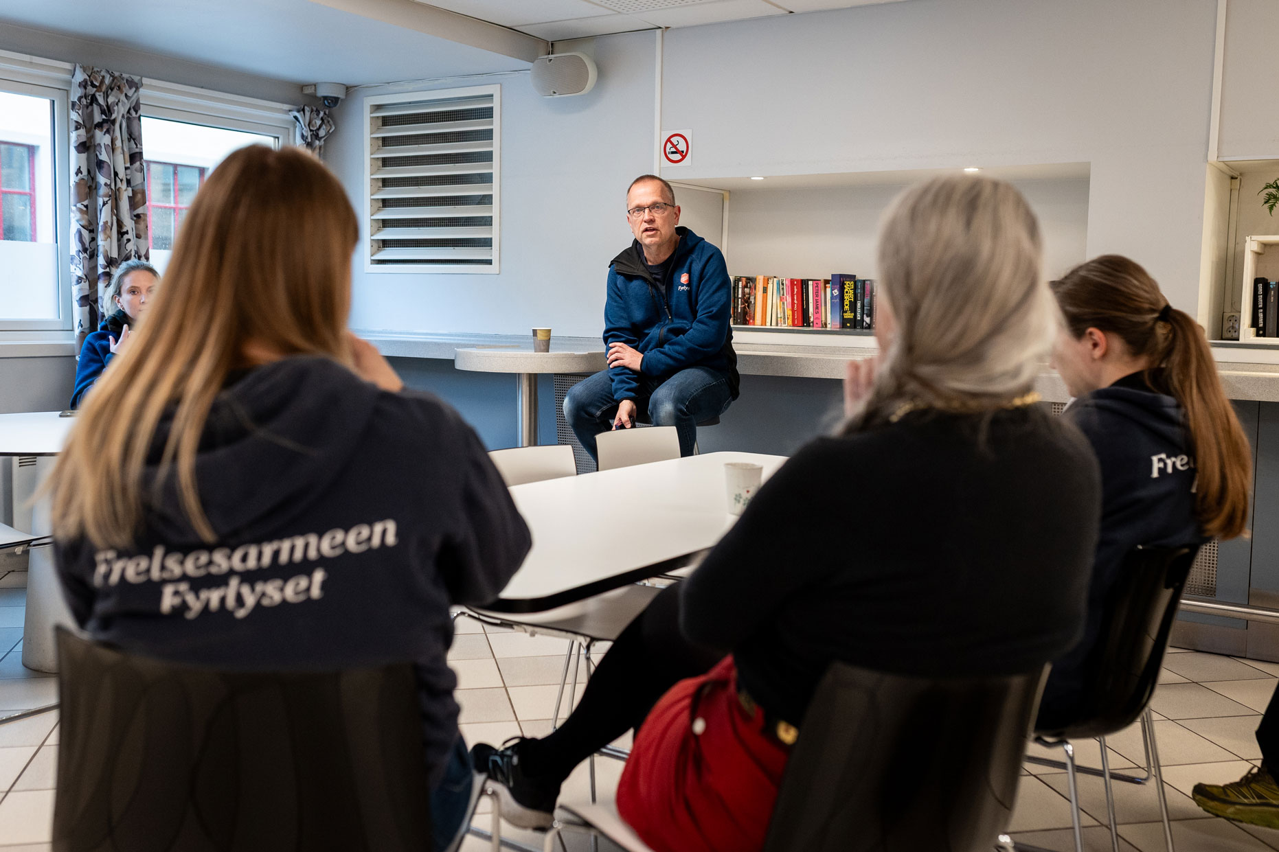 Foto: En mann sitter ved enden av et bord. I forgrunnen ser man flere personer.