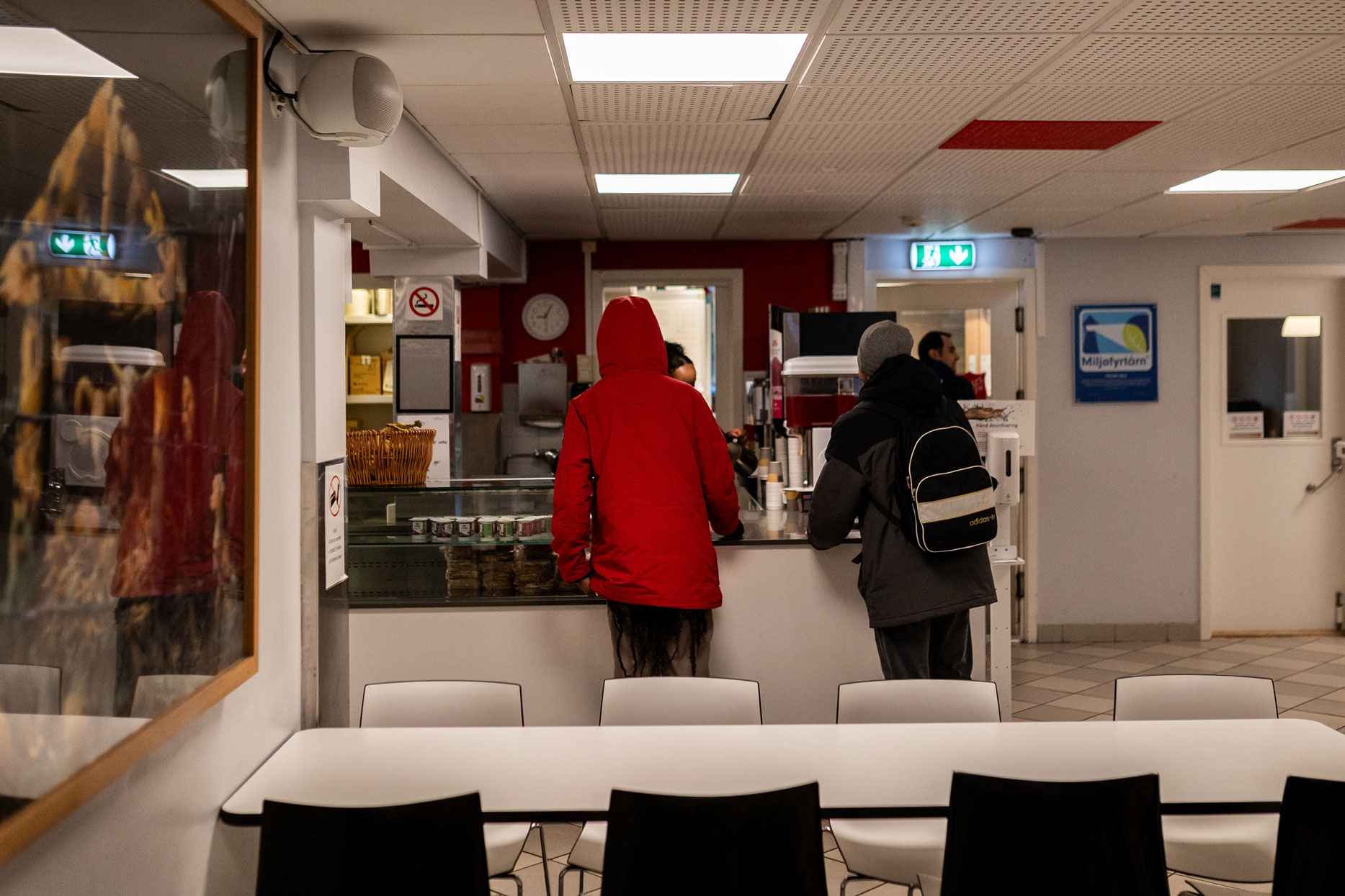 Foto: To personer i ytterjakker – en rød og en svart – står ved en disk inne i et lokale.