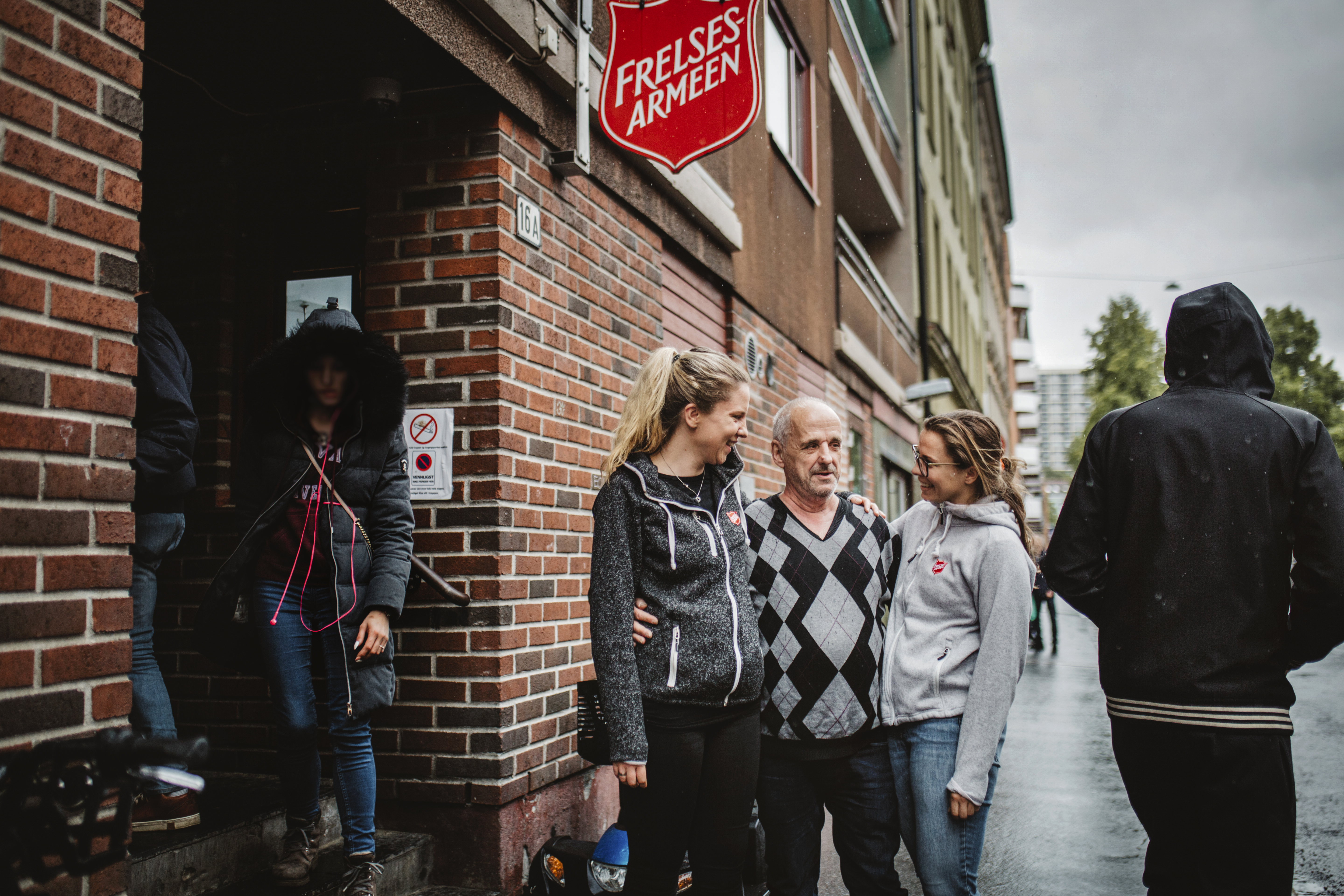 En mann står og holder rundt to ansatte ved Fyrlyset i Oslo.