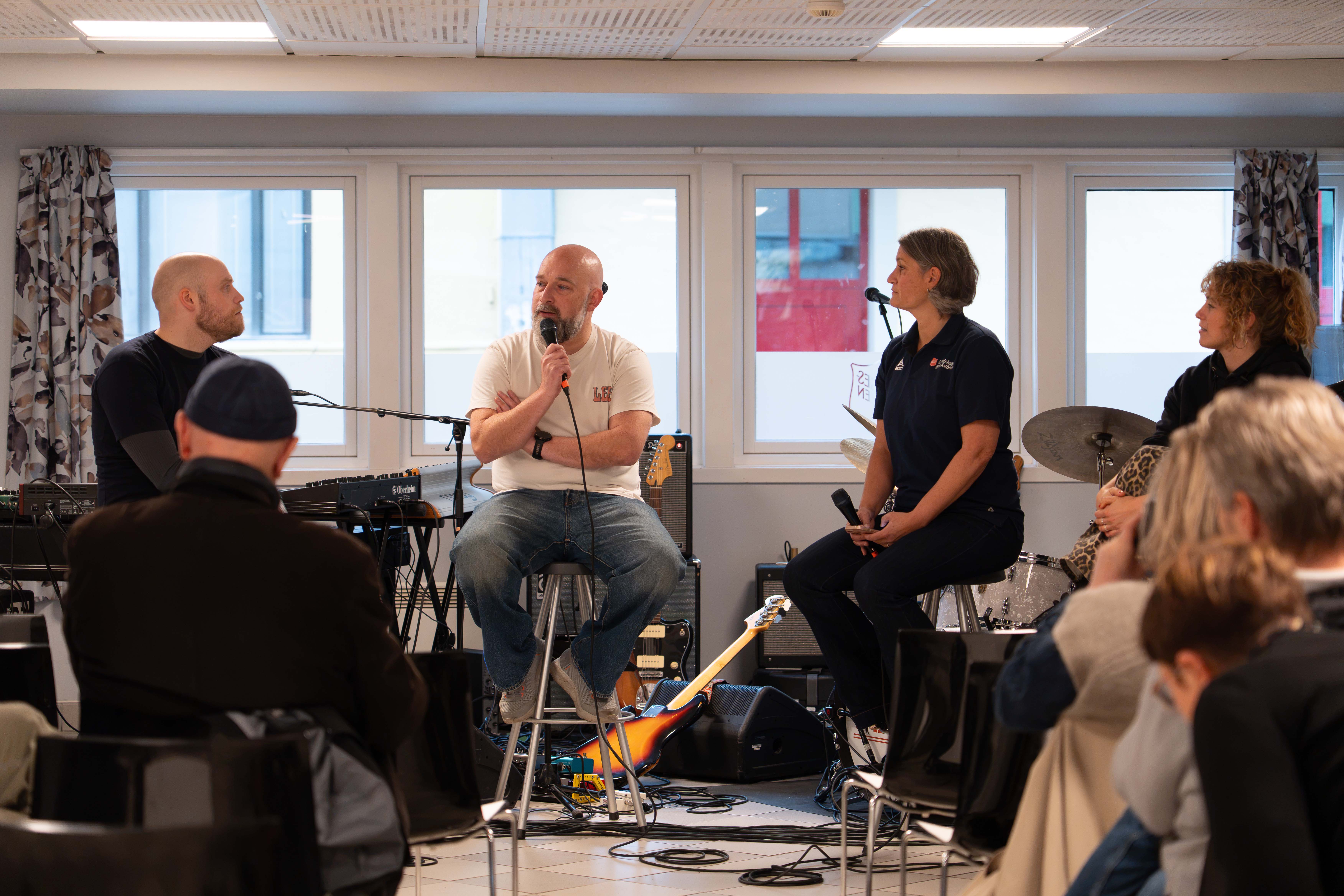 Fire mennesker, to menn og to kvinner sitter på hver sin barstol. Alle har en mikrofon i hånden og lokasjonen er Frelsesarmeens kontaktsenter for rusavhengige, Fyrlyset. Vi ser et vidu i bakgrunnen med gardiner trukket vekk. I forgrunnen skimtes noen publikummere fra anledningen at Gatepodden, en podkast om rus, lanseres.