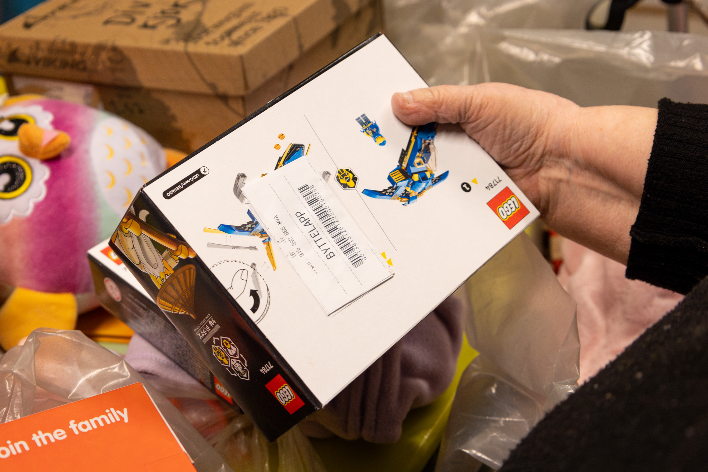 Foto: Hånd som holder to Lego-esker med byttelapp. I bakgrunnen sees andre leker, plastposer og esker.