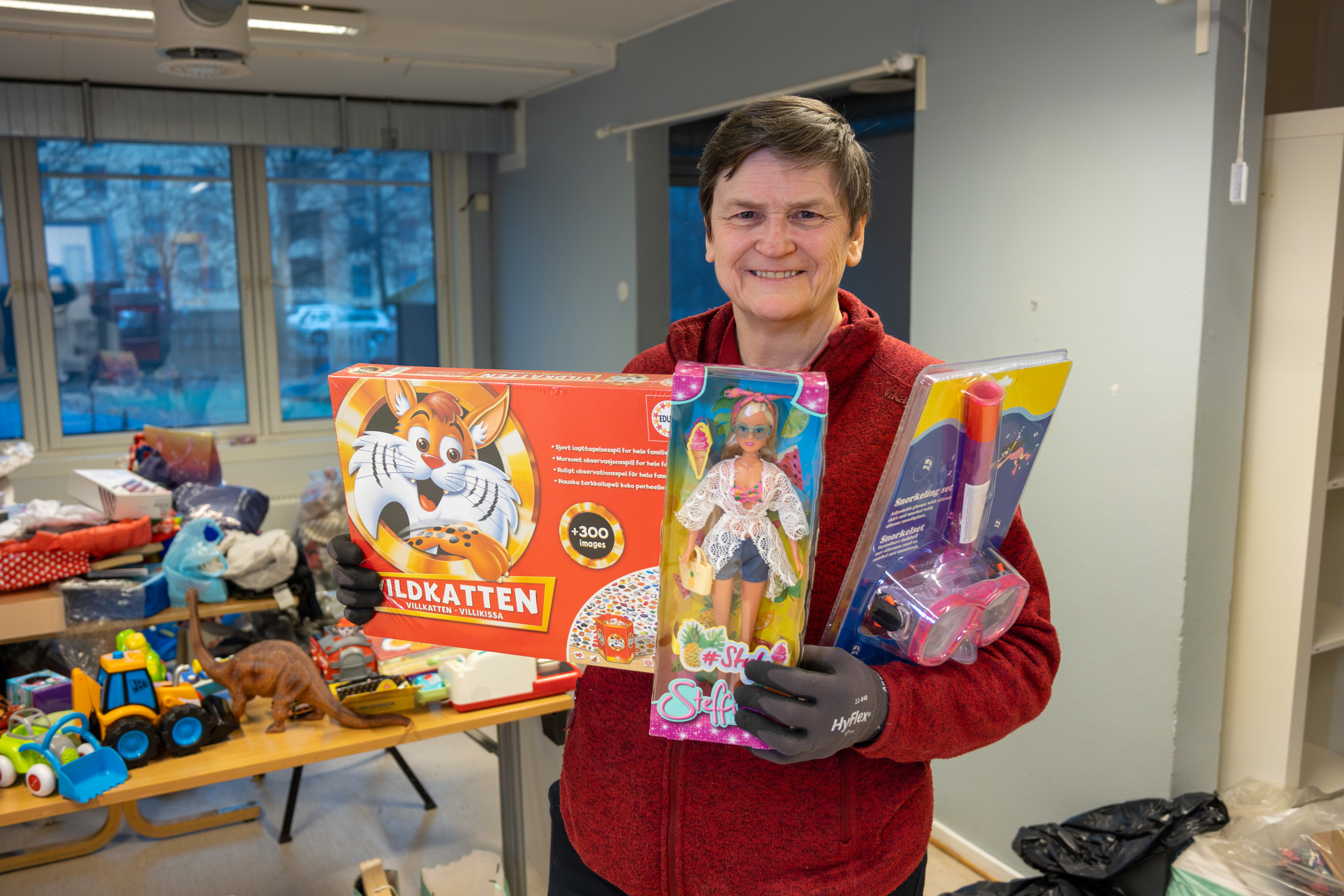 Foto: Kvinne i 60-årene med tre ulike gaver til barn smiler. Ingen av gavene er pakket inn.