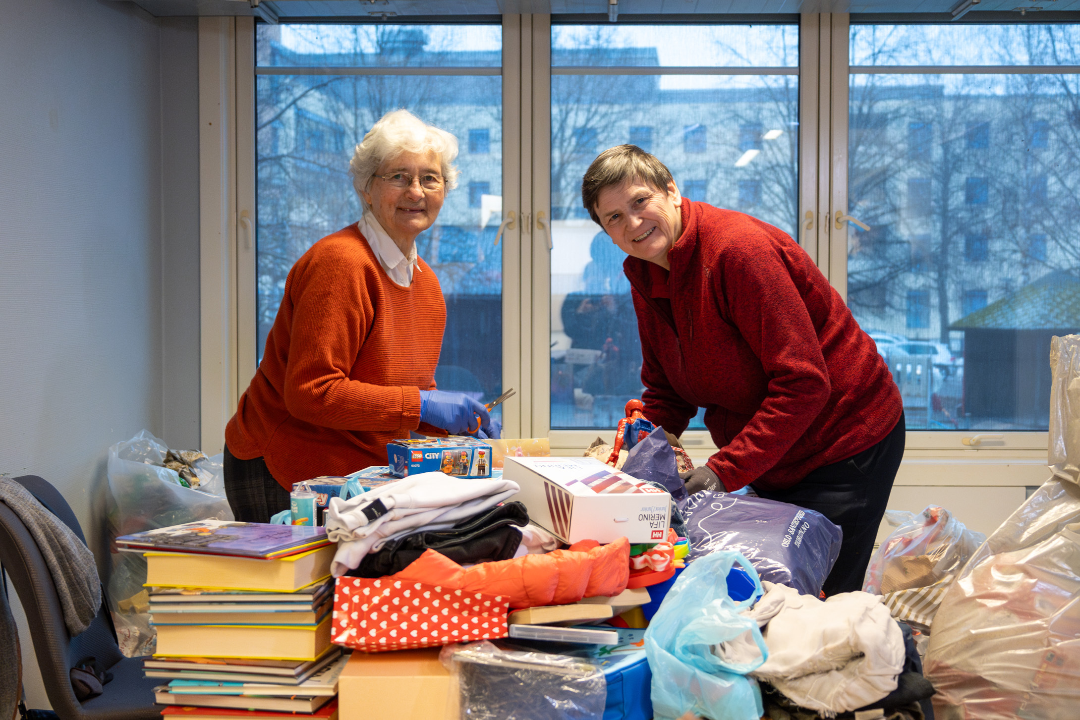 Foto: To pensjonerte damer står bøyd over et lavt bord og pakker ut julegaver.