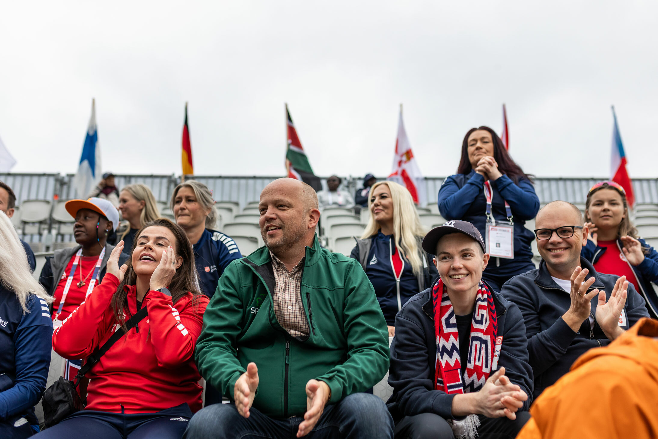 Foto: Mann i 50-årene med glattbarbert hode sitter på en tribune full av folk. De ser alle på en fotballkamp. Han har på seg grønn jakke og klapper ivrig.