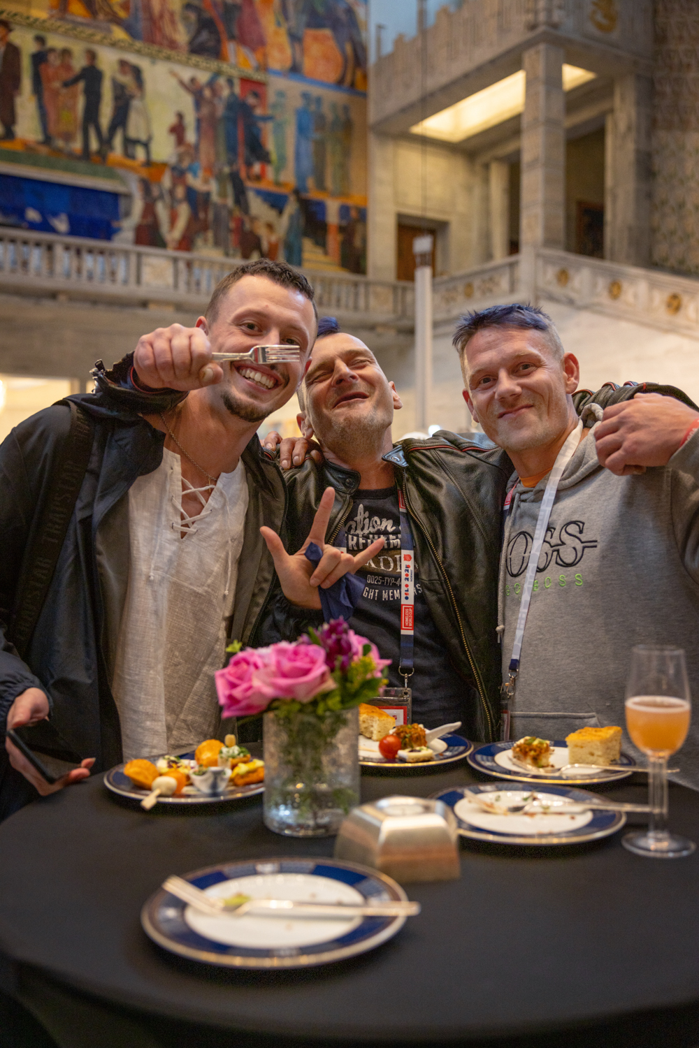 Foto: Tre svært glade menn i 30- og 40-årene, to av dem med blått hår for anledningen. De har kledd seg opp til Rådhuset og har på skinnjakker. De ser ut for å elske maten. En av dem jubler med en gaffel i hånden.