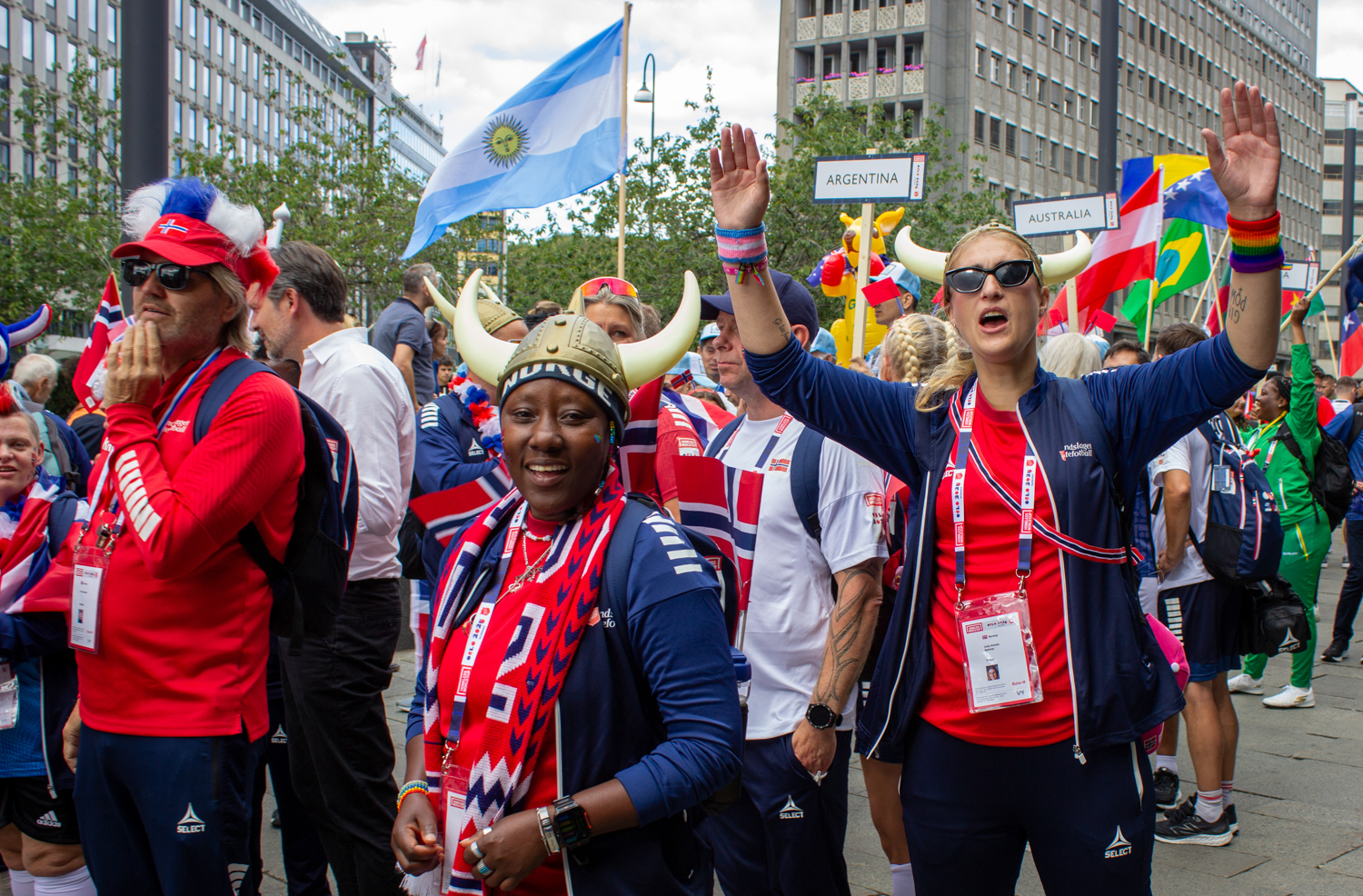 Foto: Kvinner og menn i røde, norske drakter går i tog. De er synlig glade. Hender opp i været og gøyale hatter.