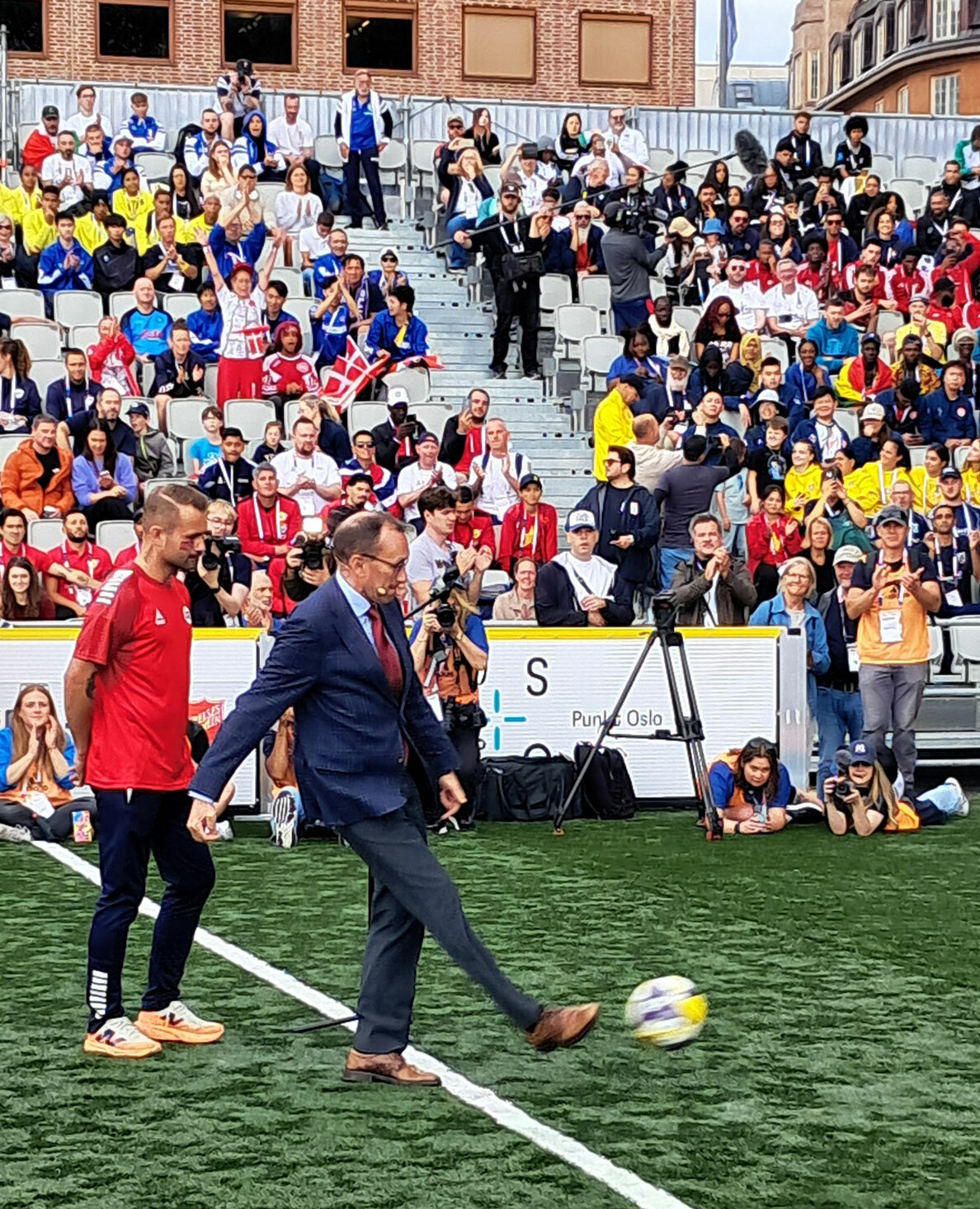 Foto: Mann i 50-årene i dress med litt lite, mørkt hår opå toppen og briller. Han sparker en ball i fart.