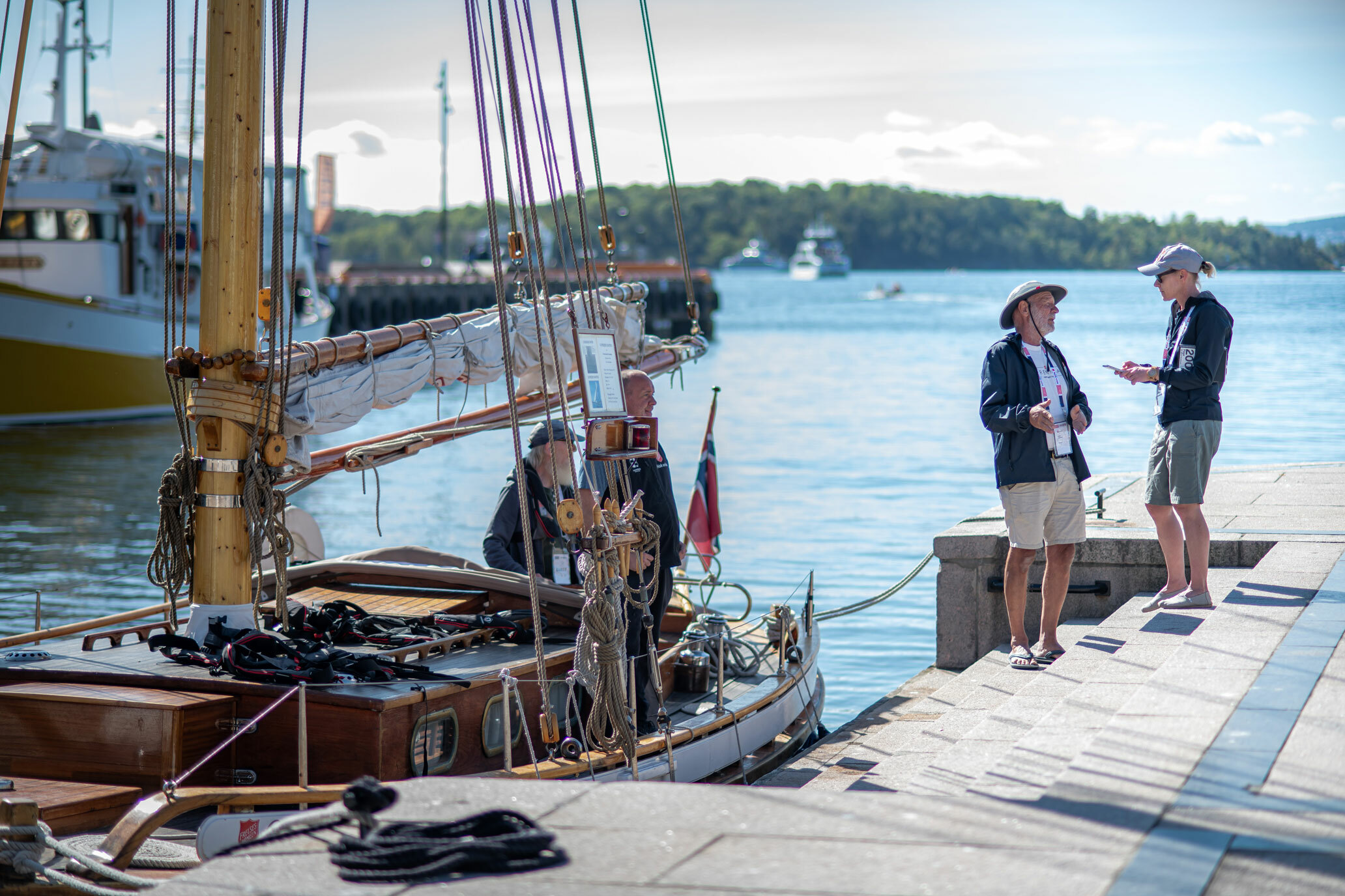 Foto: Seilbåt ligger til kai. Der står en mann med hatt og en kvinne med caps mot hverandre.