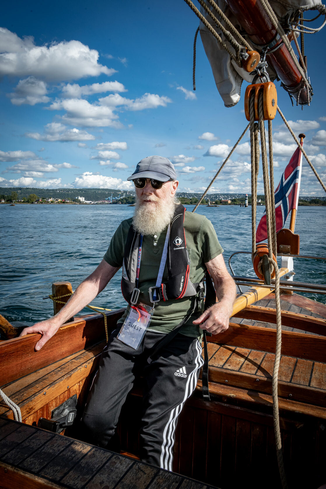 Foto: Mann med skjegg styrer en gammel seilskute. Han holder i roret.