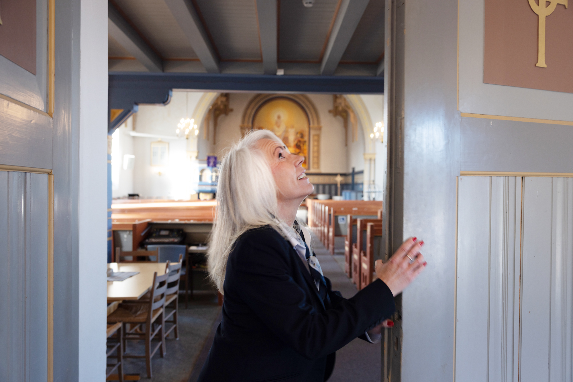 Kvinne med blondt hår åpner en dobbel dør inn til en kirkesal.