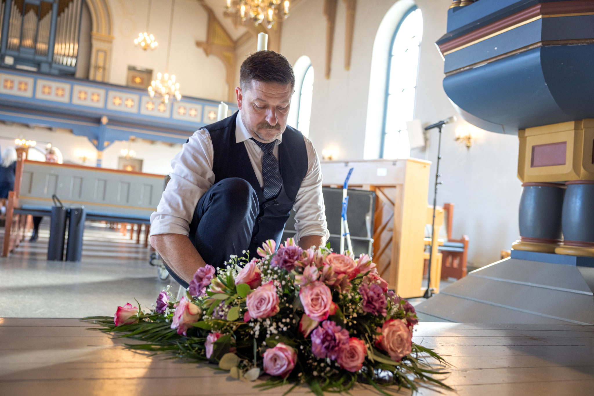 Mann med barn danderer en blomsterbukett med rosa roser like nedenfor prekestolen i en kirke.