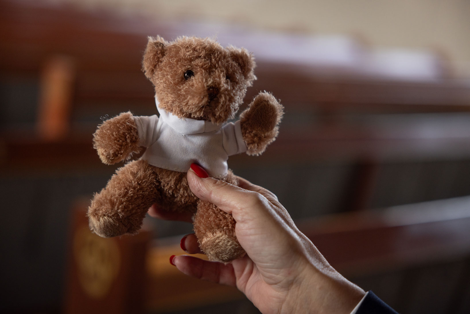 Kvinnehånd holder opp en liten, brun kosebamse med hvit hettegenser.