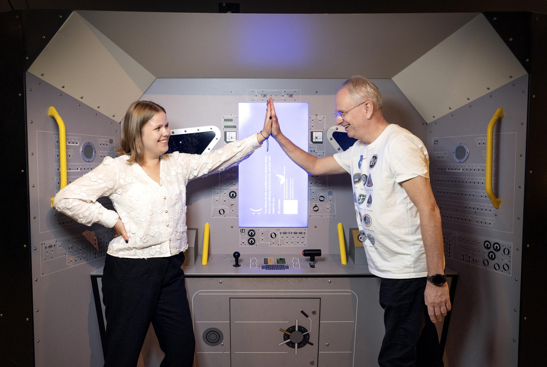 Foto: Mann i hvit T-skjorte med briller gir ung kvinne high five inne i en installasjon som er en kopi av månelanderen på innsiden.