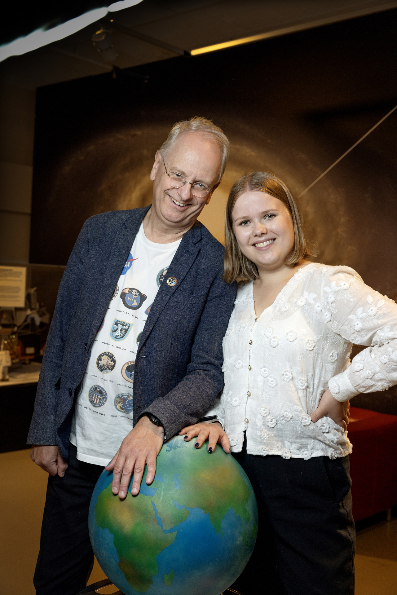 Foto: Voksen mann med briller og dressjakke holder på en globus sammen med en ung jente i hvit bluse.