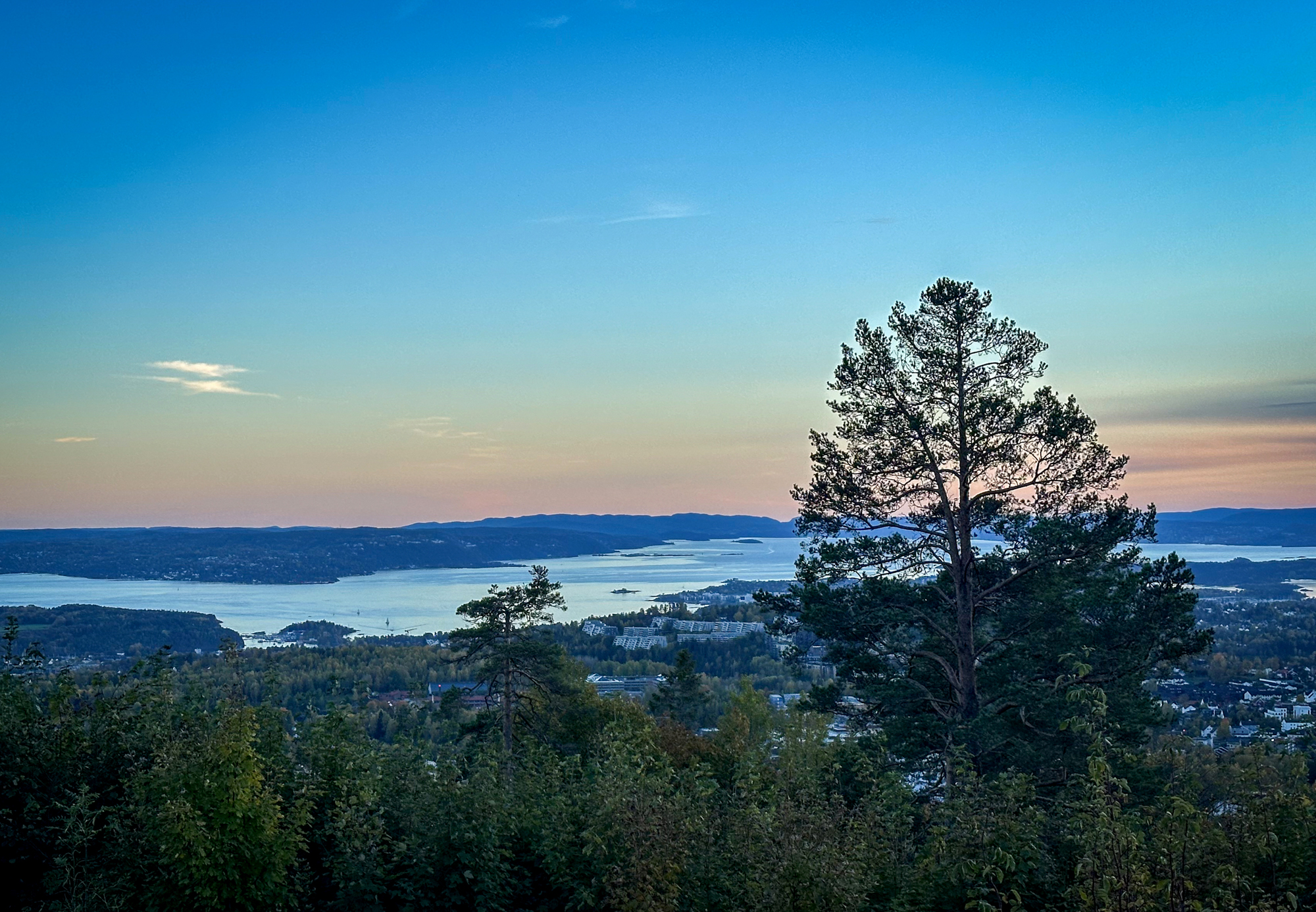 Utsikt over land og hav med rosa himmel bak.