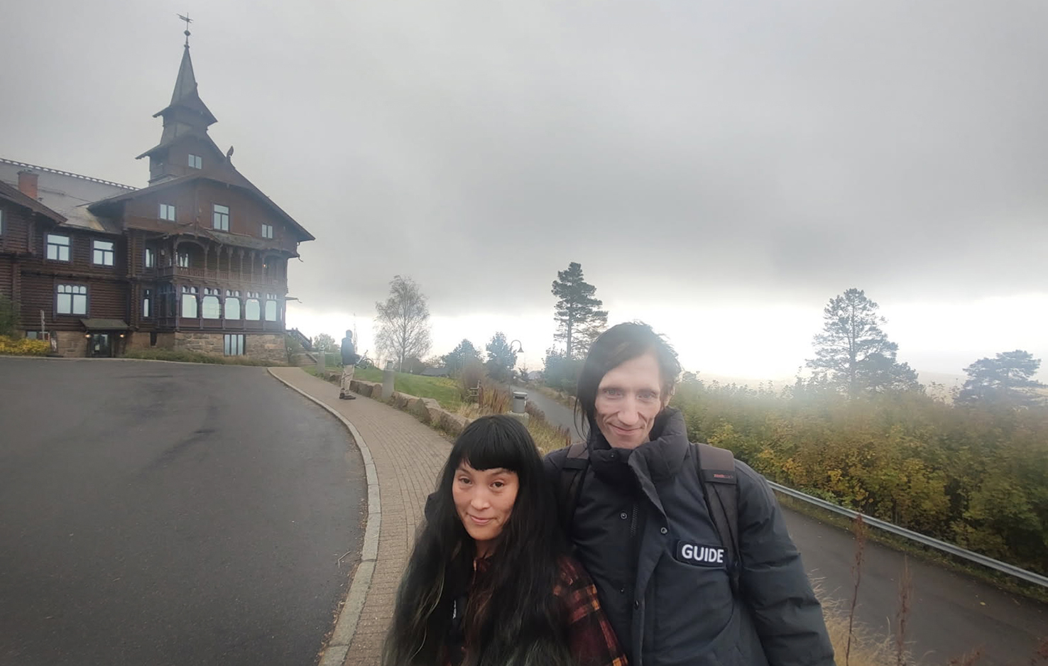 Kvinne og mann står foran et stort, gammelt brunt hus i dragestil.