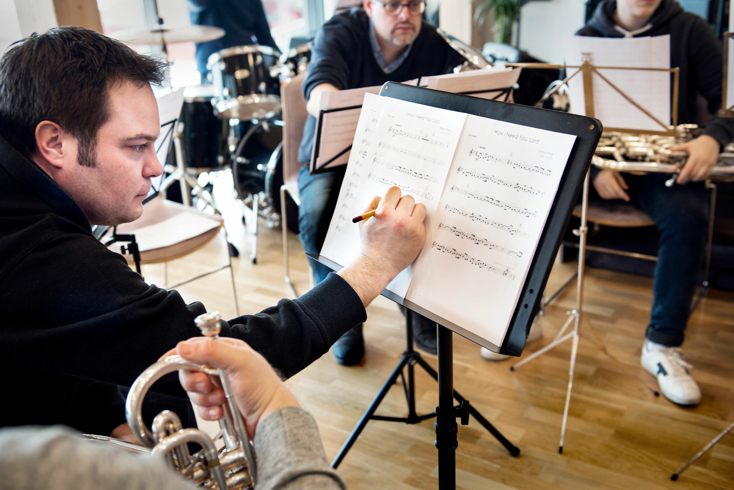 Foto: Viser tre menn som ser på noter og spiller. Kan kun se ansiktet til to av dem.