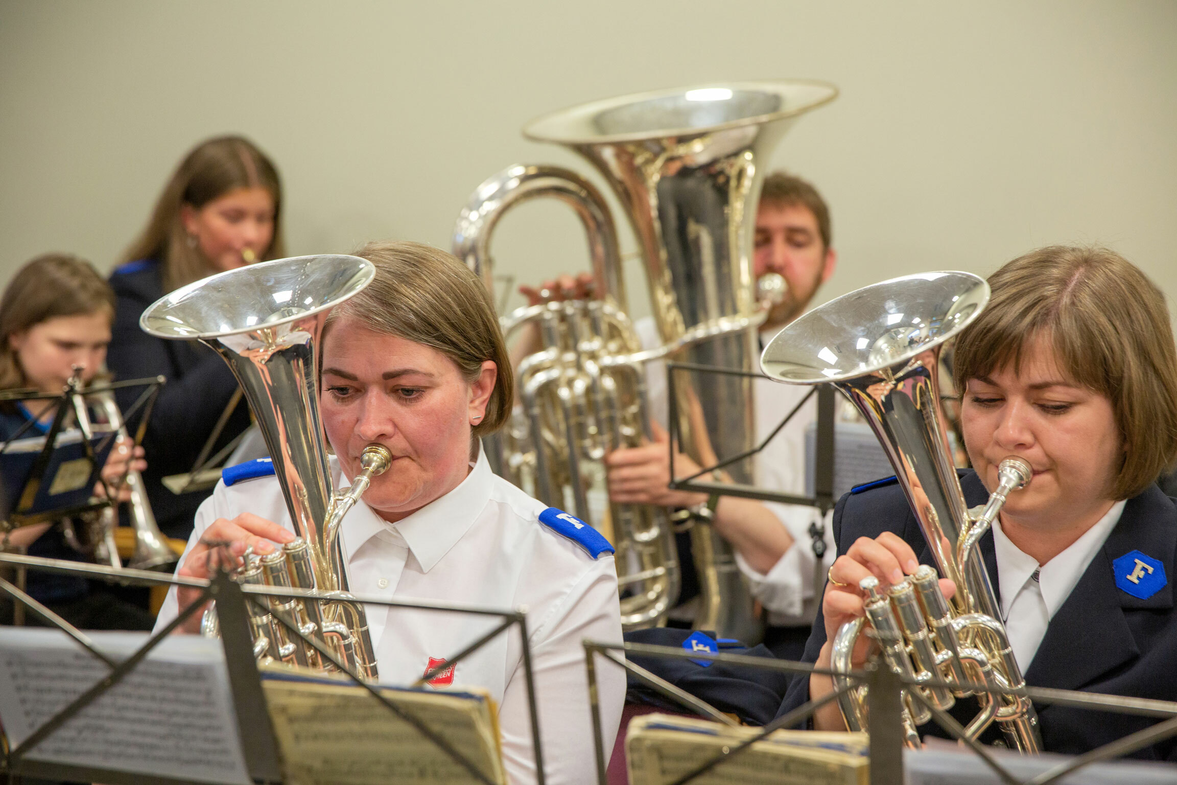 Foto: Fem personer som øver på instrumenter. Ser kun ansiktene til to voksne damer på første rekke. Begge har uniformer fra Frelsesarmeen på seg.