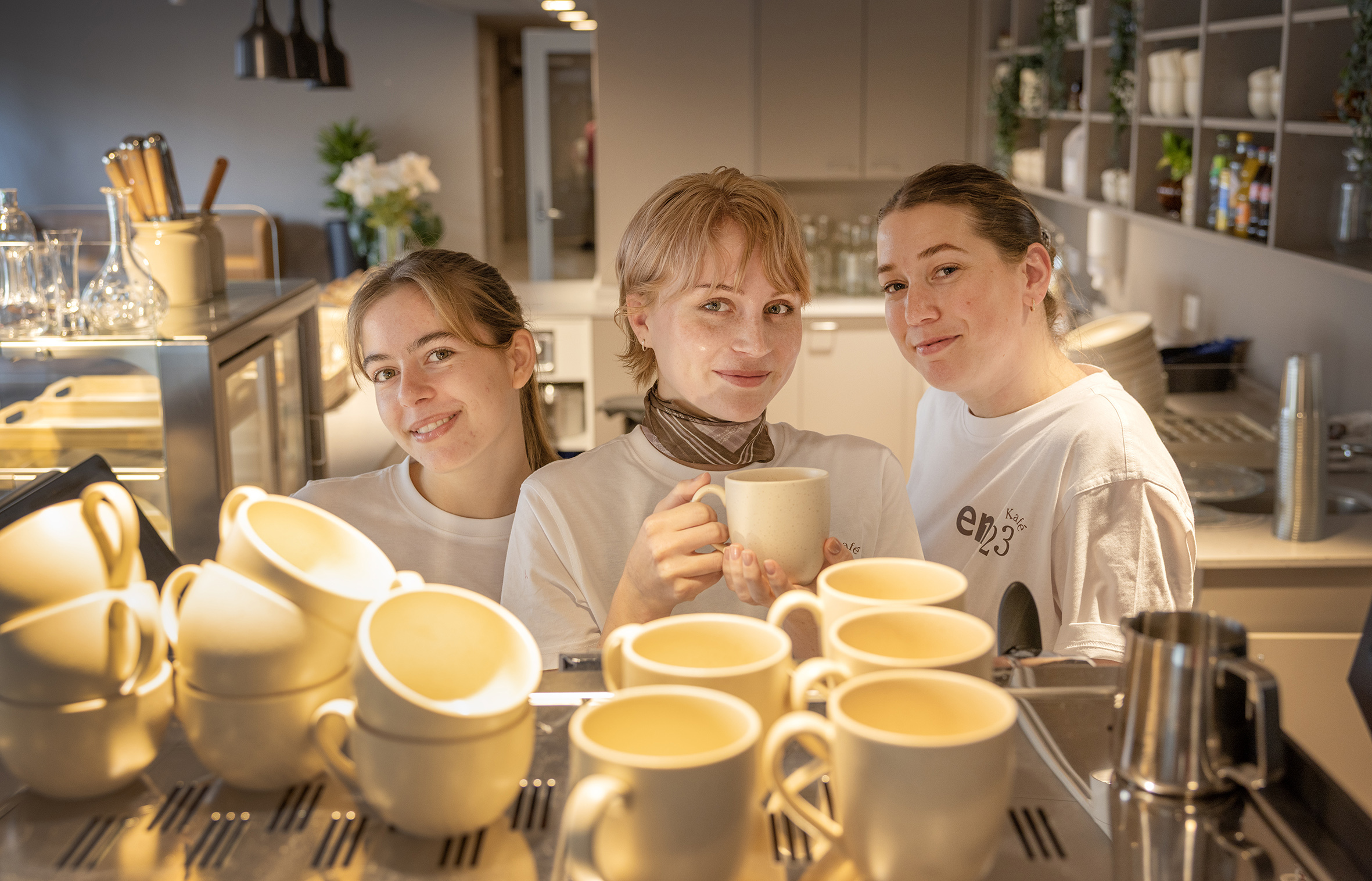 Foto: tre unge kvinner fotografert over kaffemaskinen.