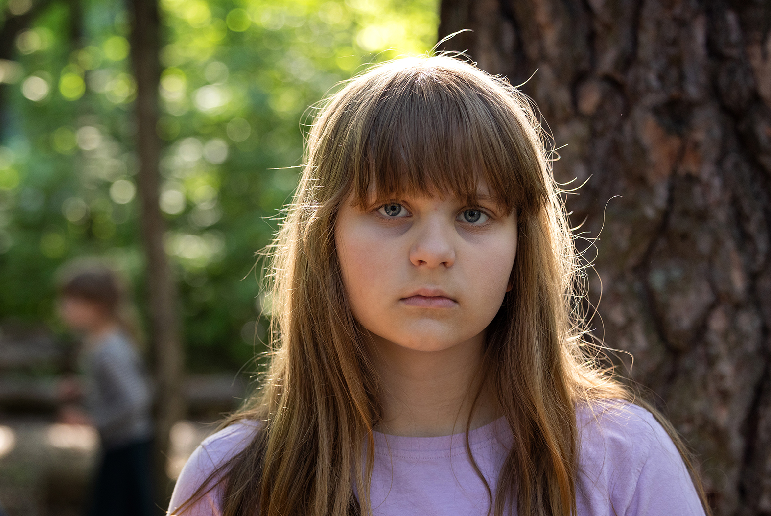 Bilde av skolejente som ser i kameraet, litt trist. Illustrasjonsfoto. Det er skog i bakgrunnen.