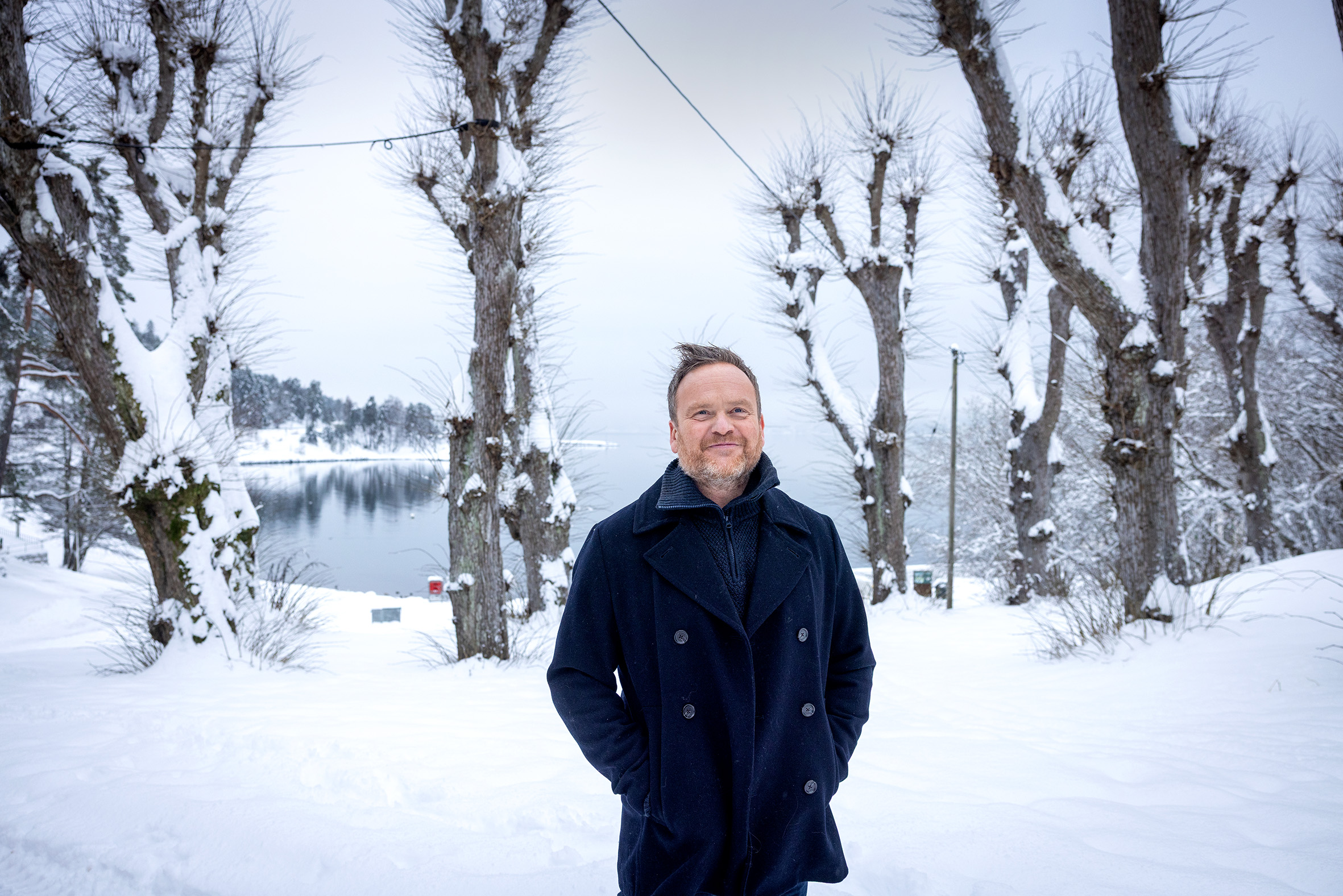 Foto: Mann i blå jakke ute i vinterlandskap med mange nakne trær.