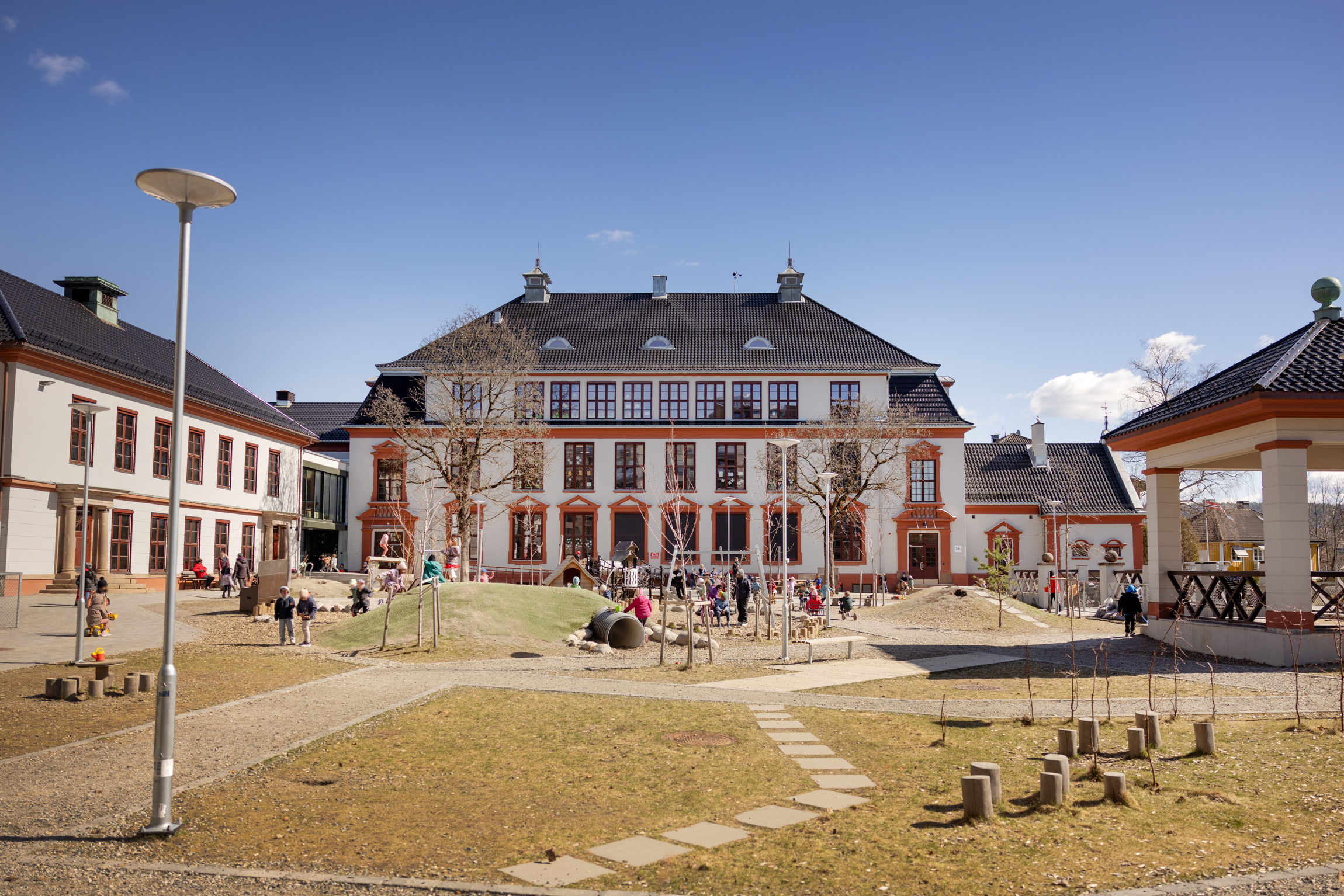 To foto: Bildet til venstre viser en gammel murbygning med et diger uteplass foran. Bildet til høyre viser flere folk sammen, der en ung mann med briller og skjegg ler sammen med to voksne, blonde damer.