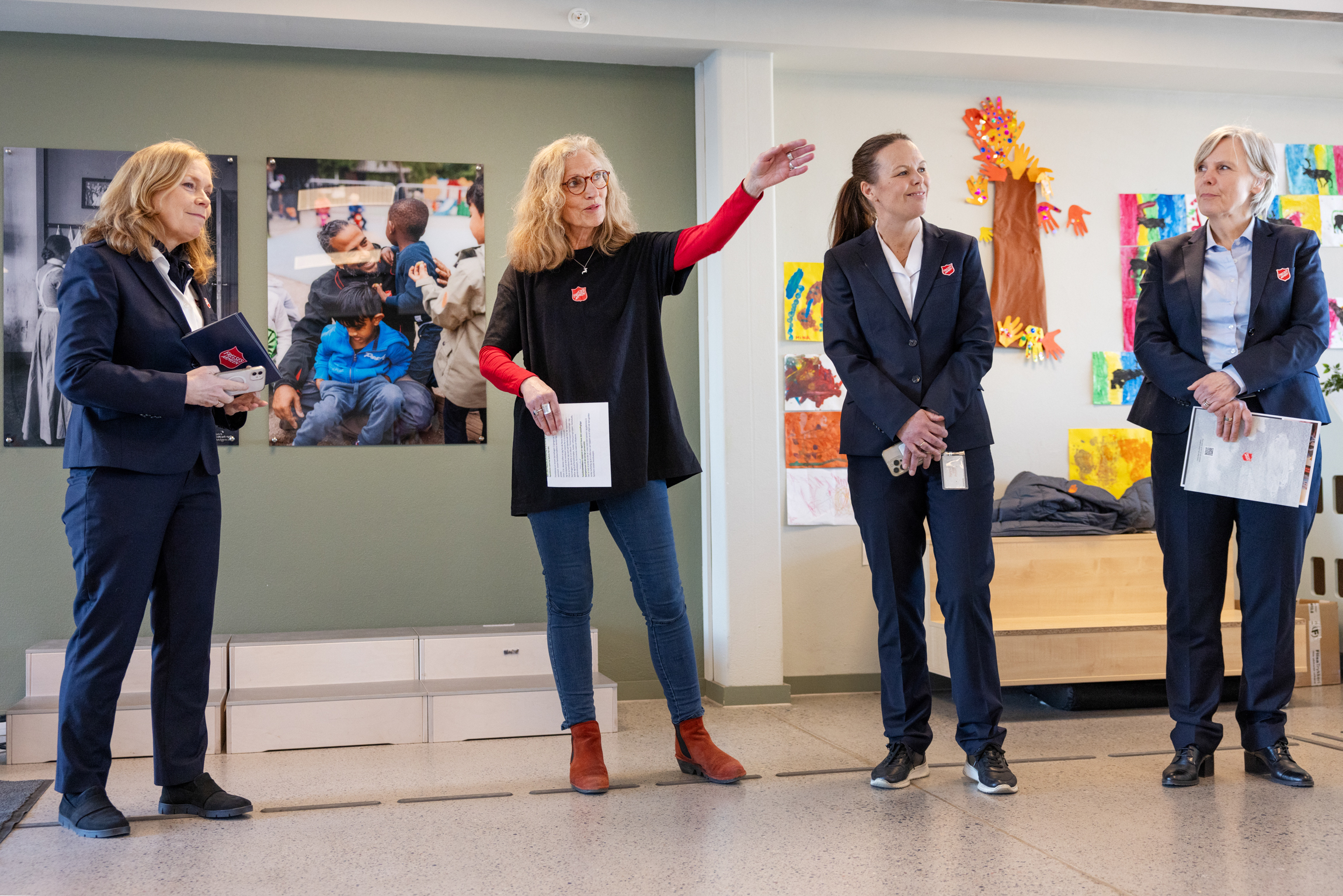 Fire kvinner står på rekke inne i en barnehage. Alle er fra Frelsesarmeen. Nummer to peker ut i rommet med venstre hånd.