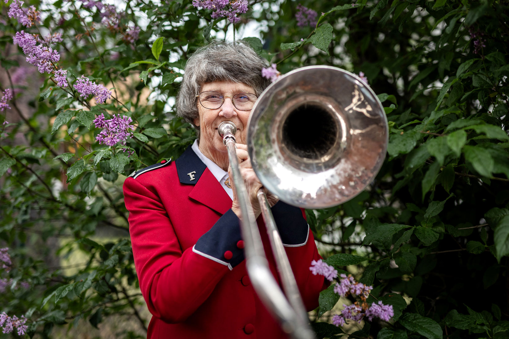 Foto: Dame med grått hår og rød musikantuniform fra Frelsesarmeen som spiller trombone.