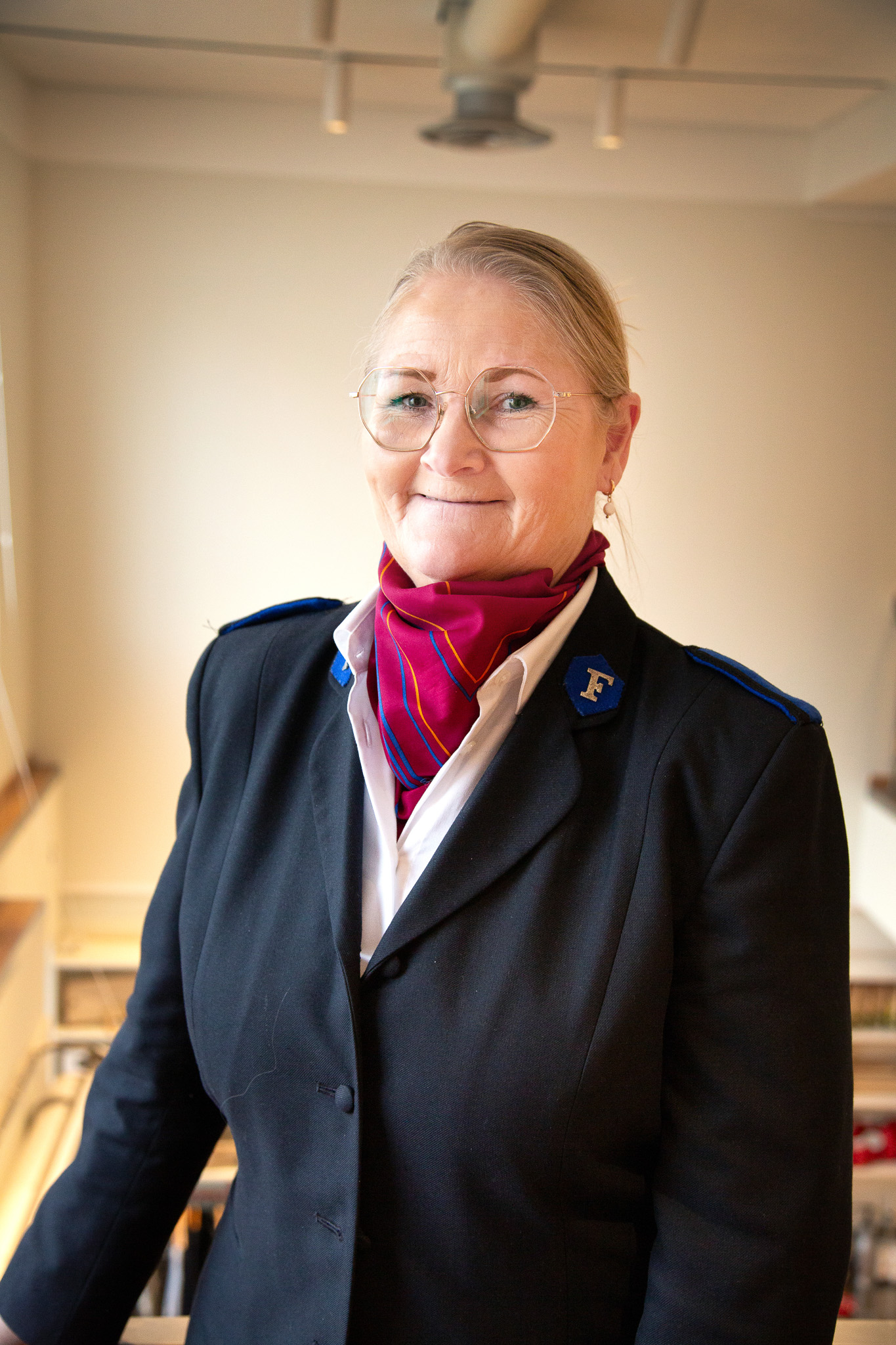 Foto: Kvinne i uniform står inne og smiler mot kamera.