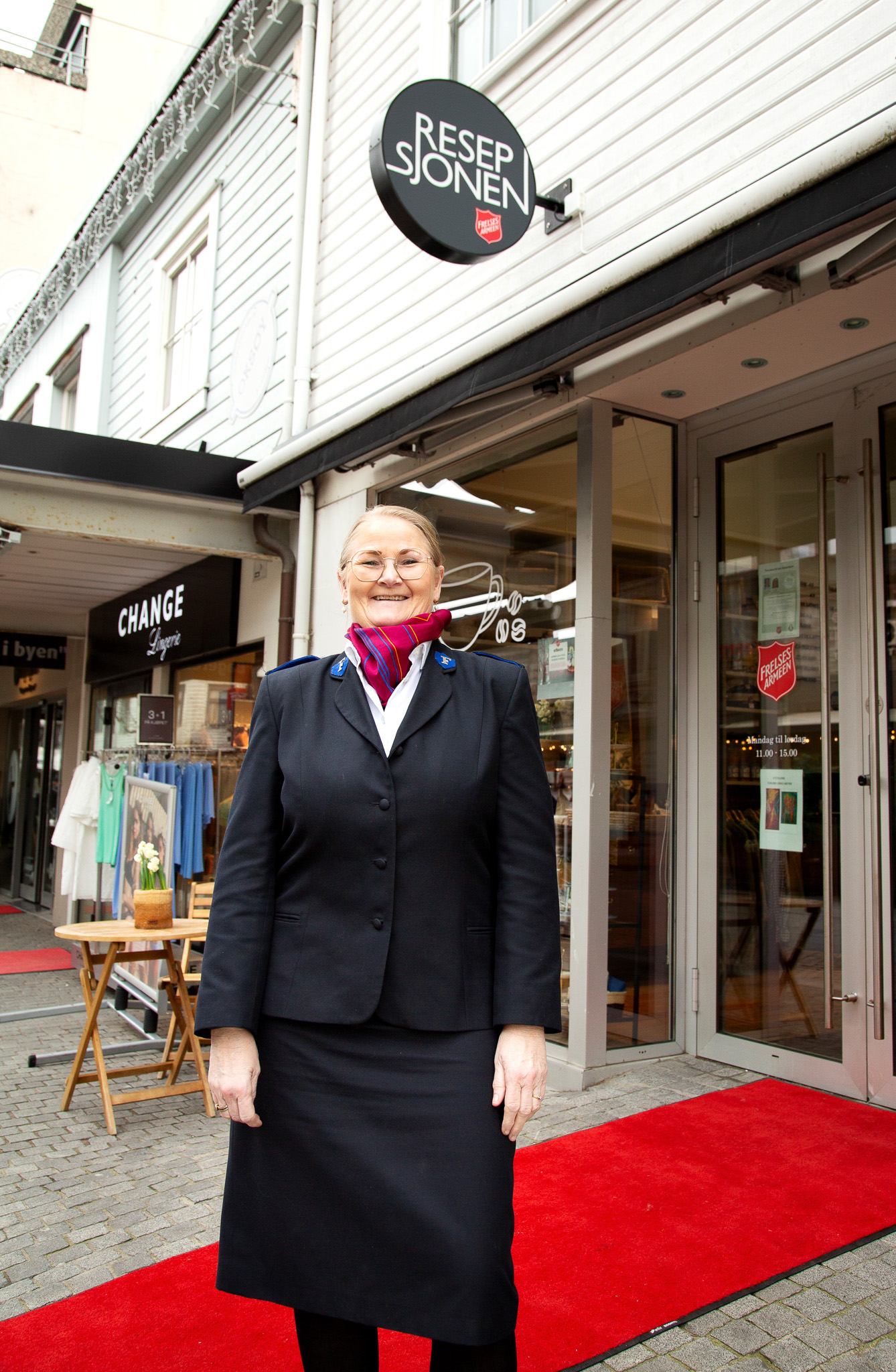 Foto: Kvinne i uniform fra Frelsesarmeen står ute foran et hvitt bygg. Det er rullet ut en rød løper inn til døra.