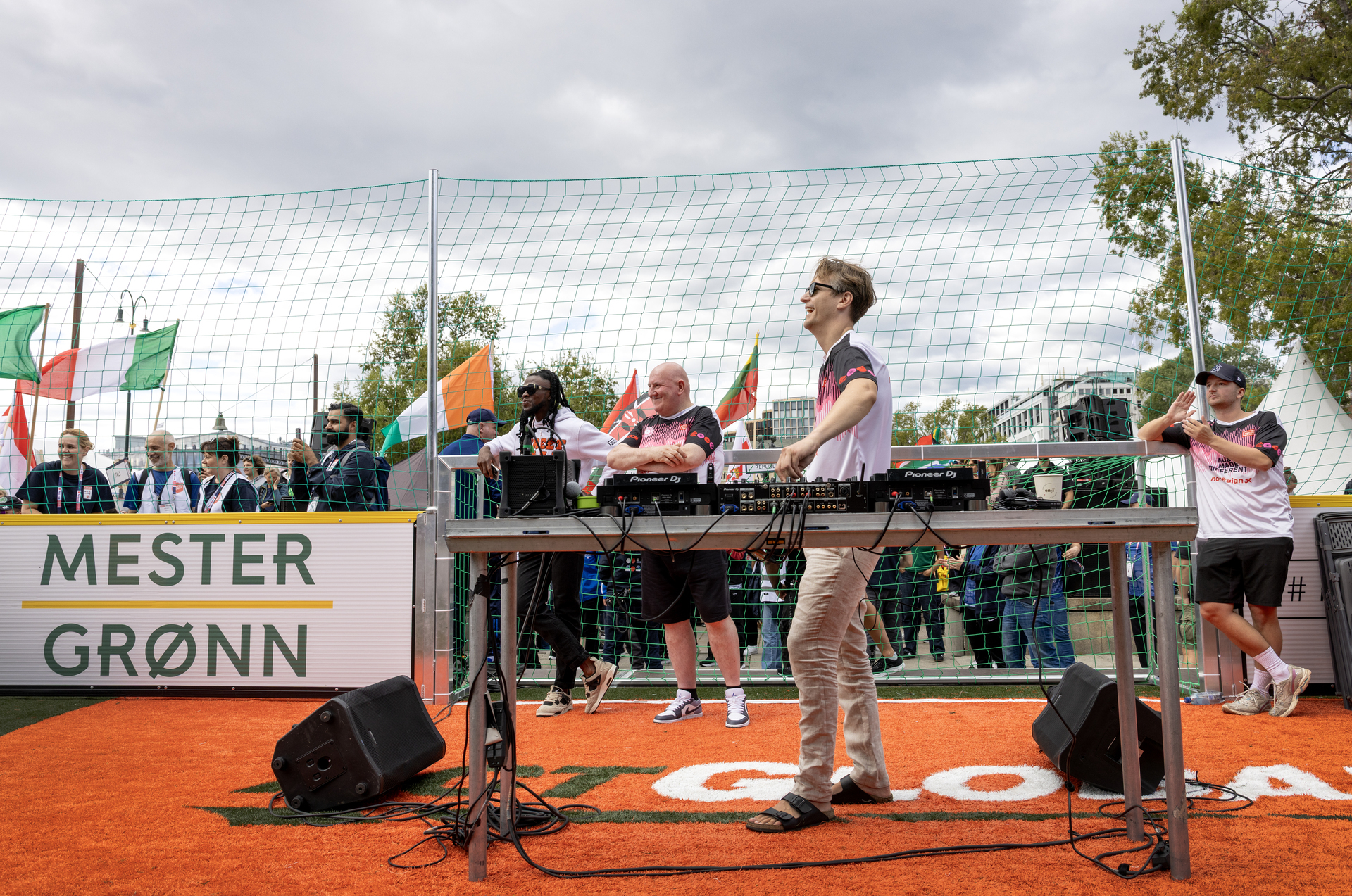 Foto: Mann ved miksepult ser utover publikum. På hver sin side av ham står to andre menn i lik T-skjorte.