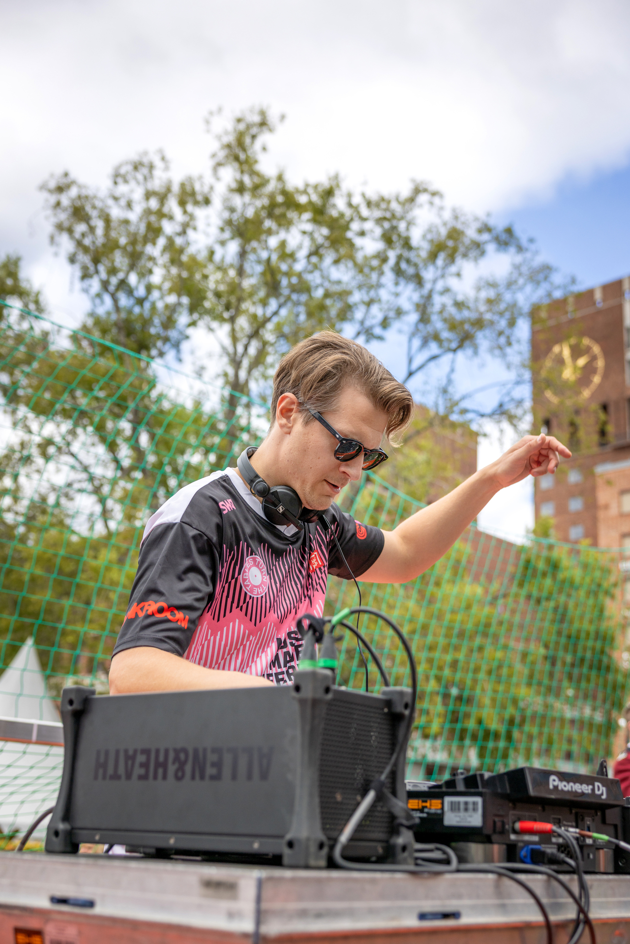 Foto: Mann med solbriller står ved en miksepult. I bakgrunnen sees grønne trær og klokka på det ene tårnet i Oslo rådhus.