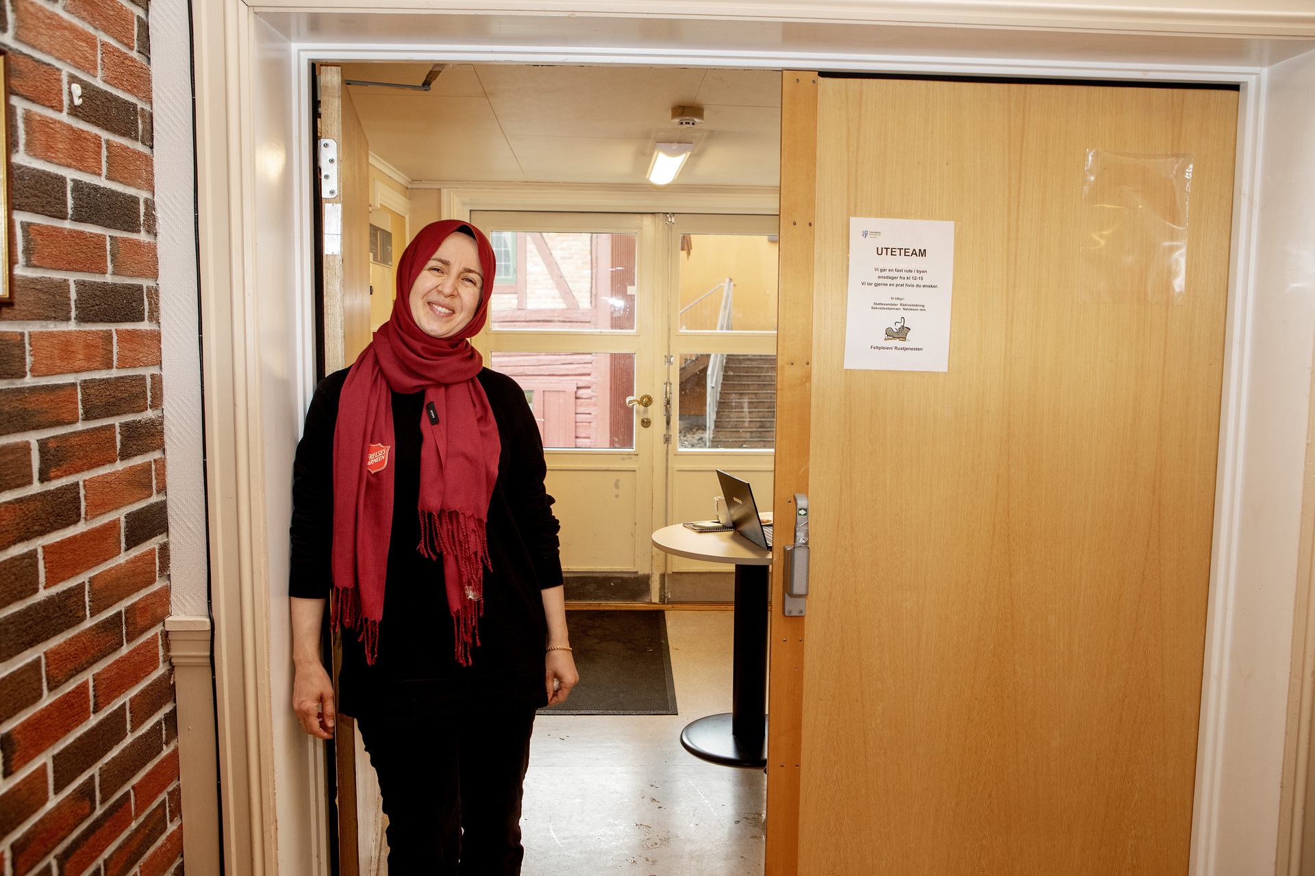 Foto: Buket står i en døråpningog smiler. Bordet ved matutdelingen kan skimtes i bakgrunnen.