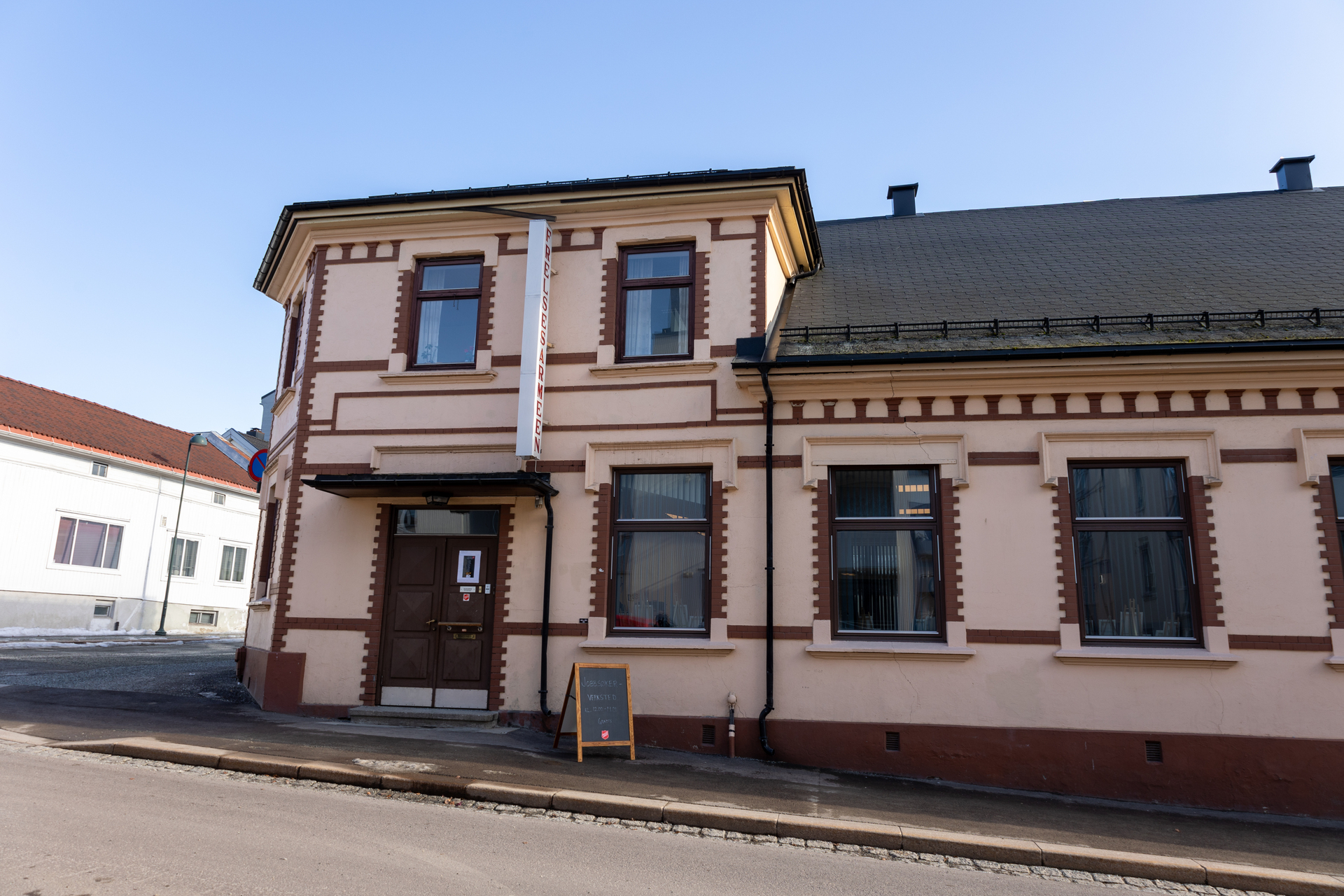 Foto: Bilde av deler av bygget til Drammen korps, tatt fra den andre siden av gata. Utenfor står en tavle med informasjon om at det er åpent jobbsøkerverksted.