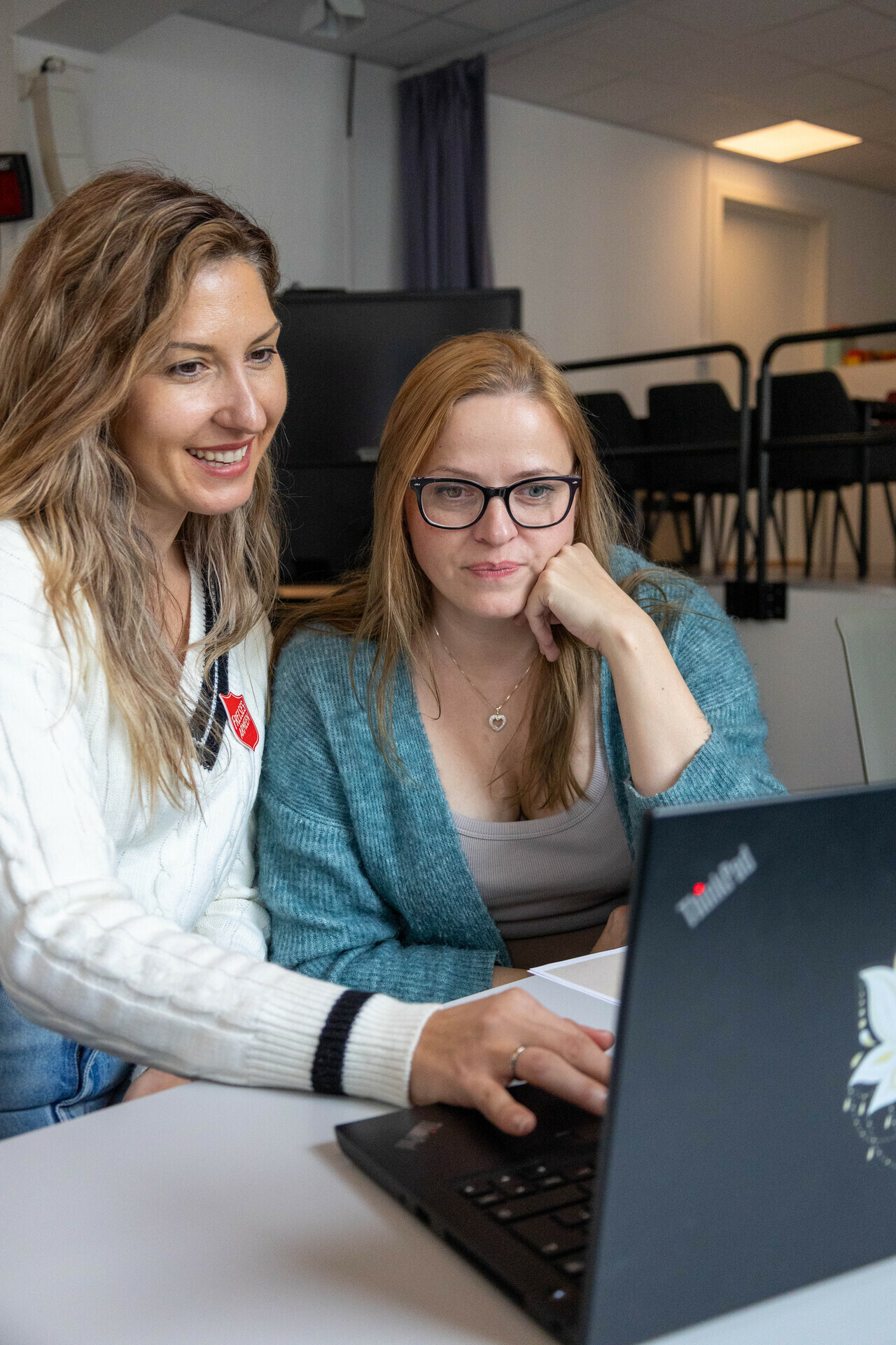 Foto: Dhurata og Inese sitter og ser mot en laptop. Dhurata trykker på tastaturet ,mens Inese hviler hodet mot en hånd og ser på skjermen.