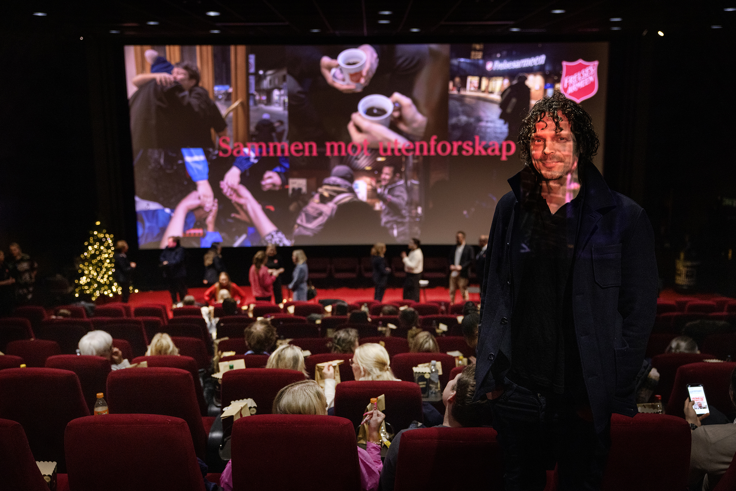 Mann i mørk kinosal. På lerretet er det en bildecollage fra Frelsesarmeen med teksten: Sammen mot utenforskap.