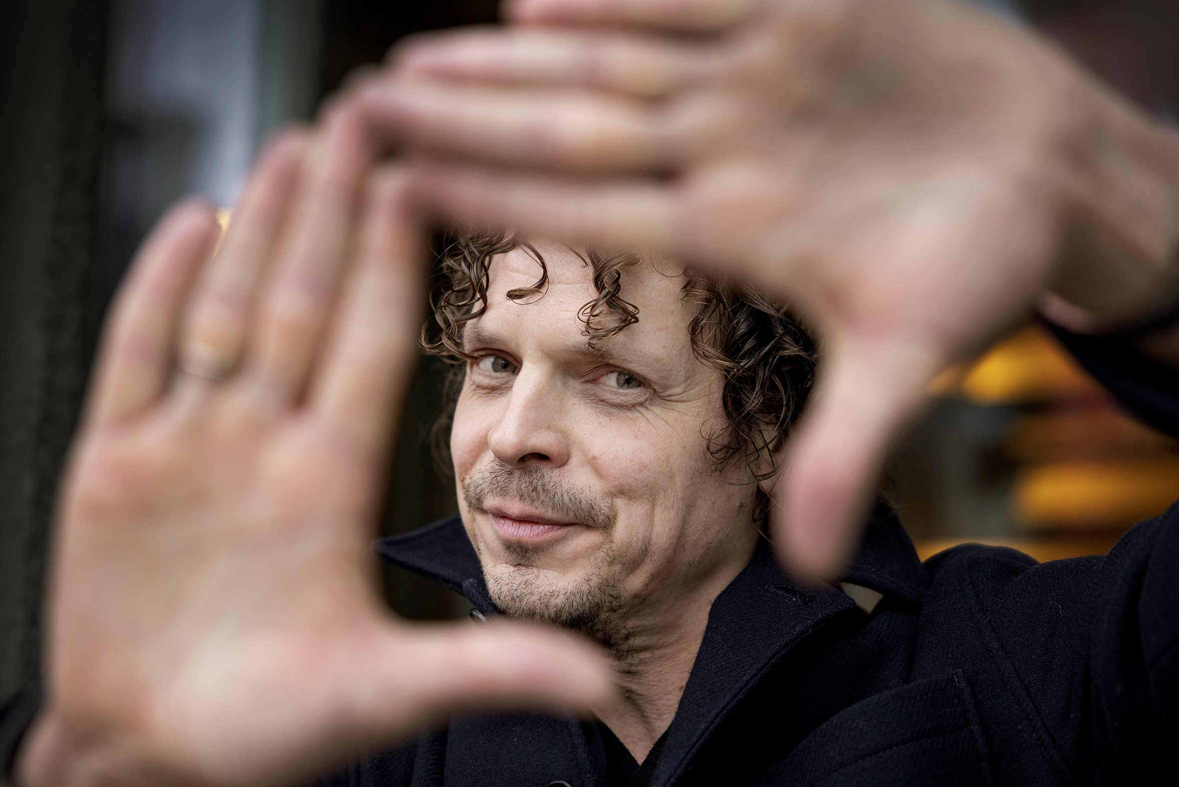 Nærbilde av mann som holder hendene i en firkant. Gjennom den ser du ansiktet hans.