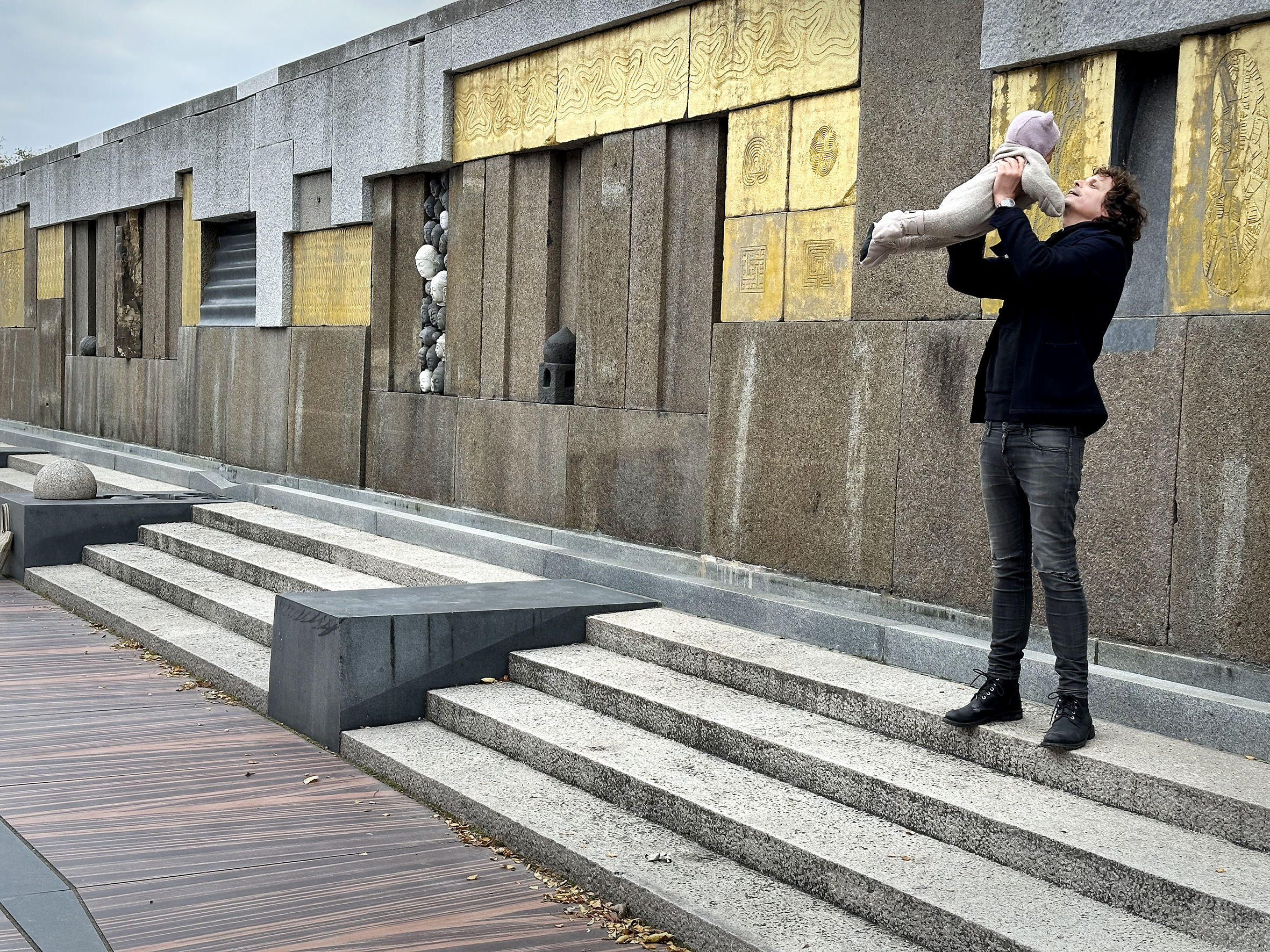 Mann med datter som han svinger opp i lufta. Utsmykket område med trapper og store blokker i stein dekorert med gullelementer.